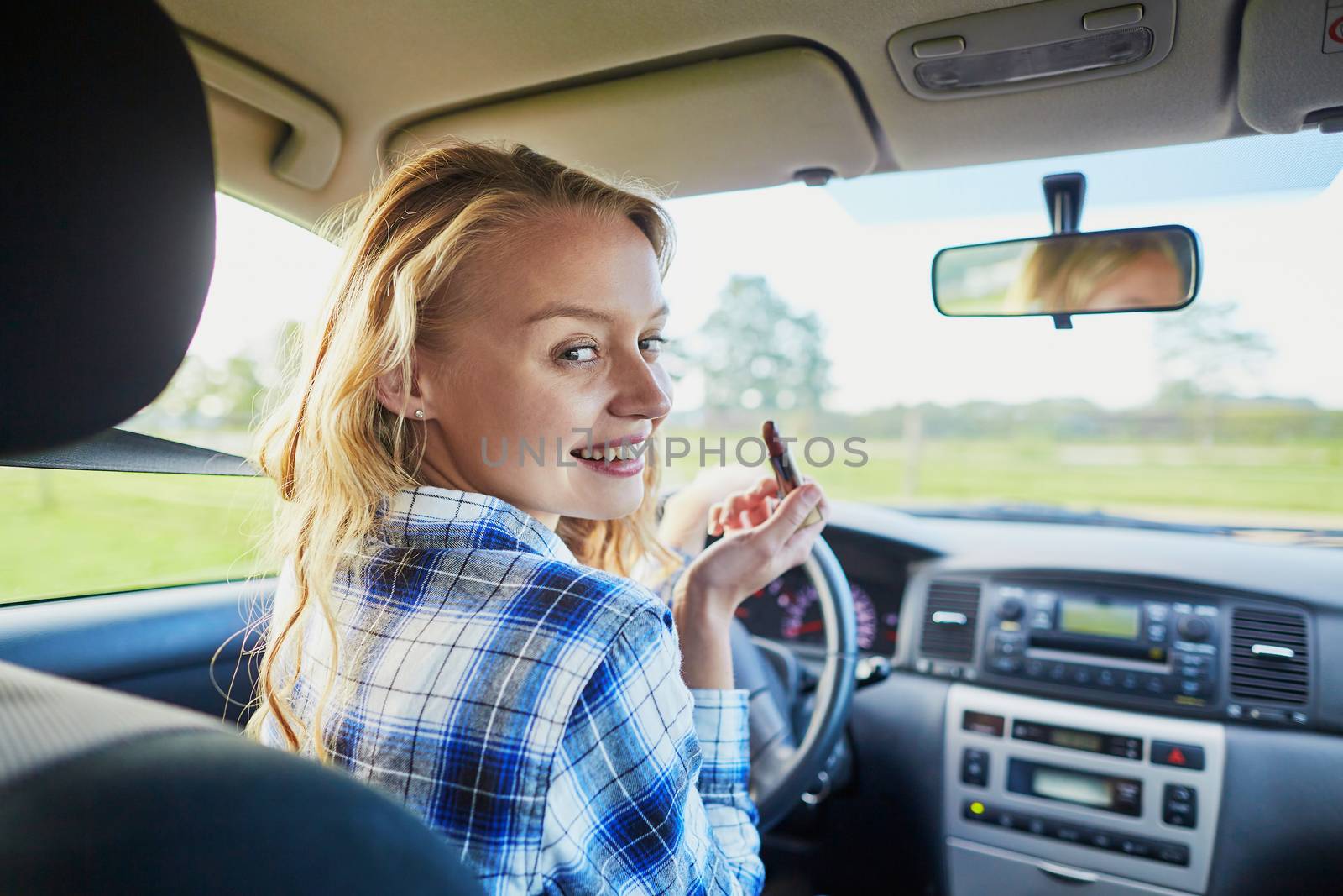Beautiful blond woman applying lipstick in a car while driving