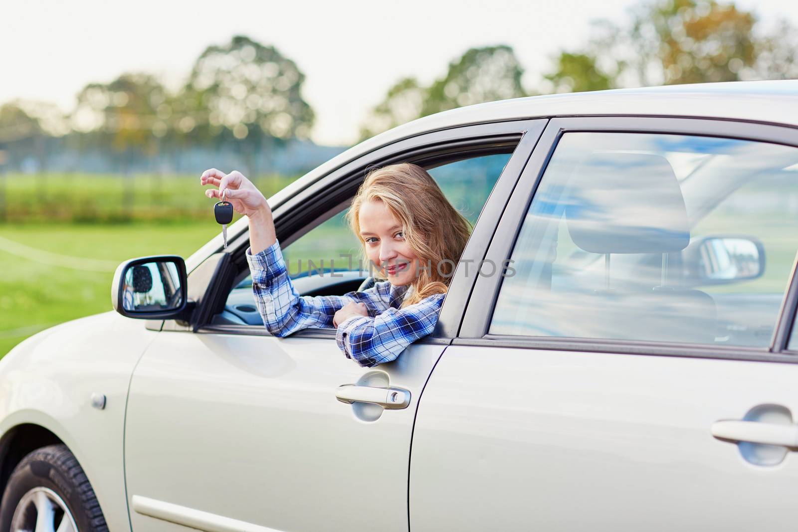 Beautiful young driver looking out of the car window holding a key