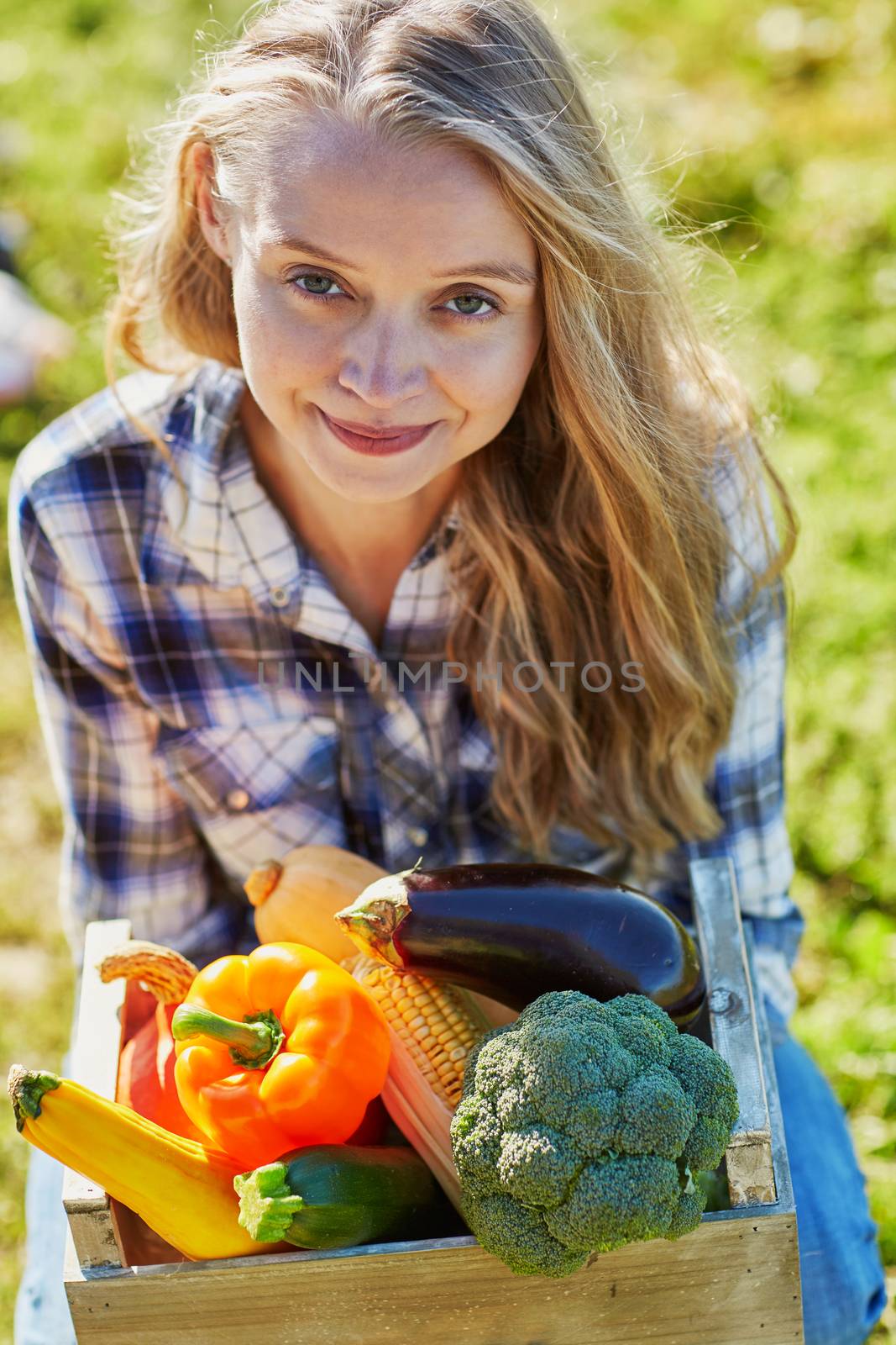Happy young woman holding wooden crate with fresh organic vegetables from farm