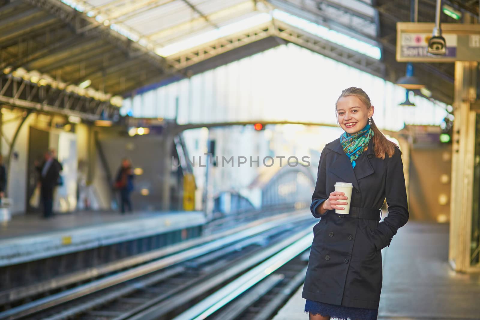 Beautiful young woman waiting for a train while drinking coffee on the platform of Parisian underground