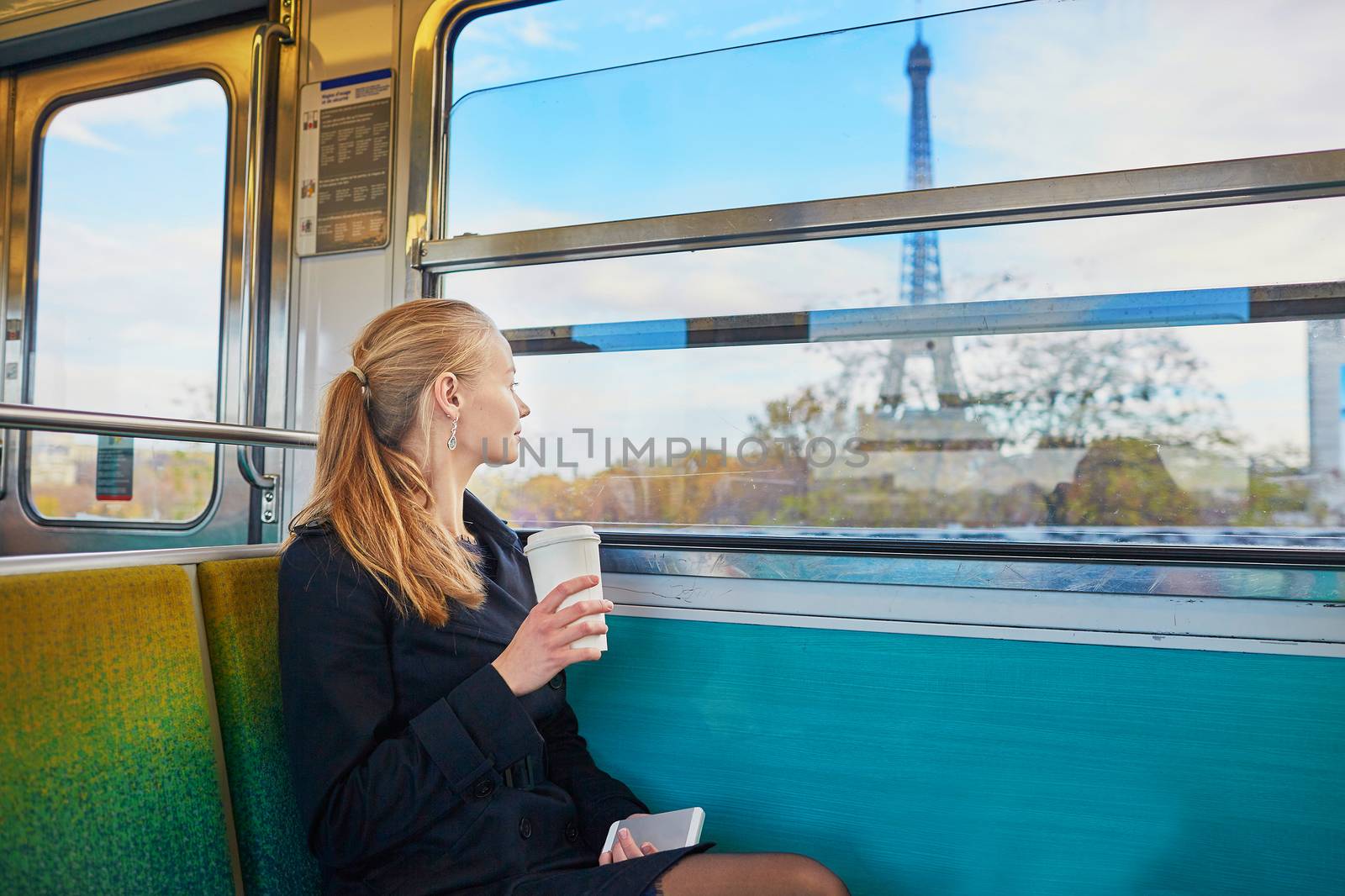 Beautiful young woman travelling in a train of Parisian underground and drinking coffee. Eiffel tower is behind the window