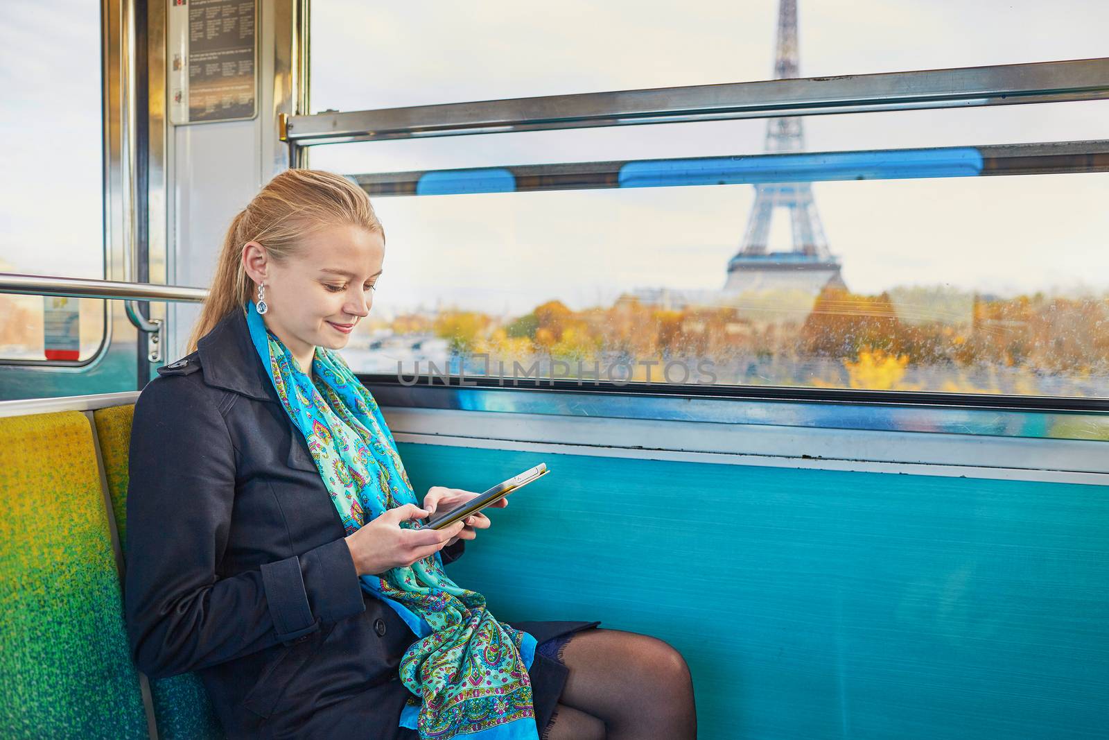 Beautiful young woman travelling in a train of Parisian underground and reading a book. Eiffel tower is behind the window