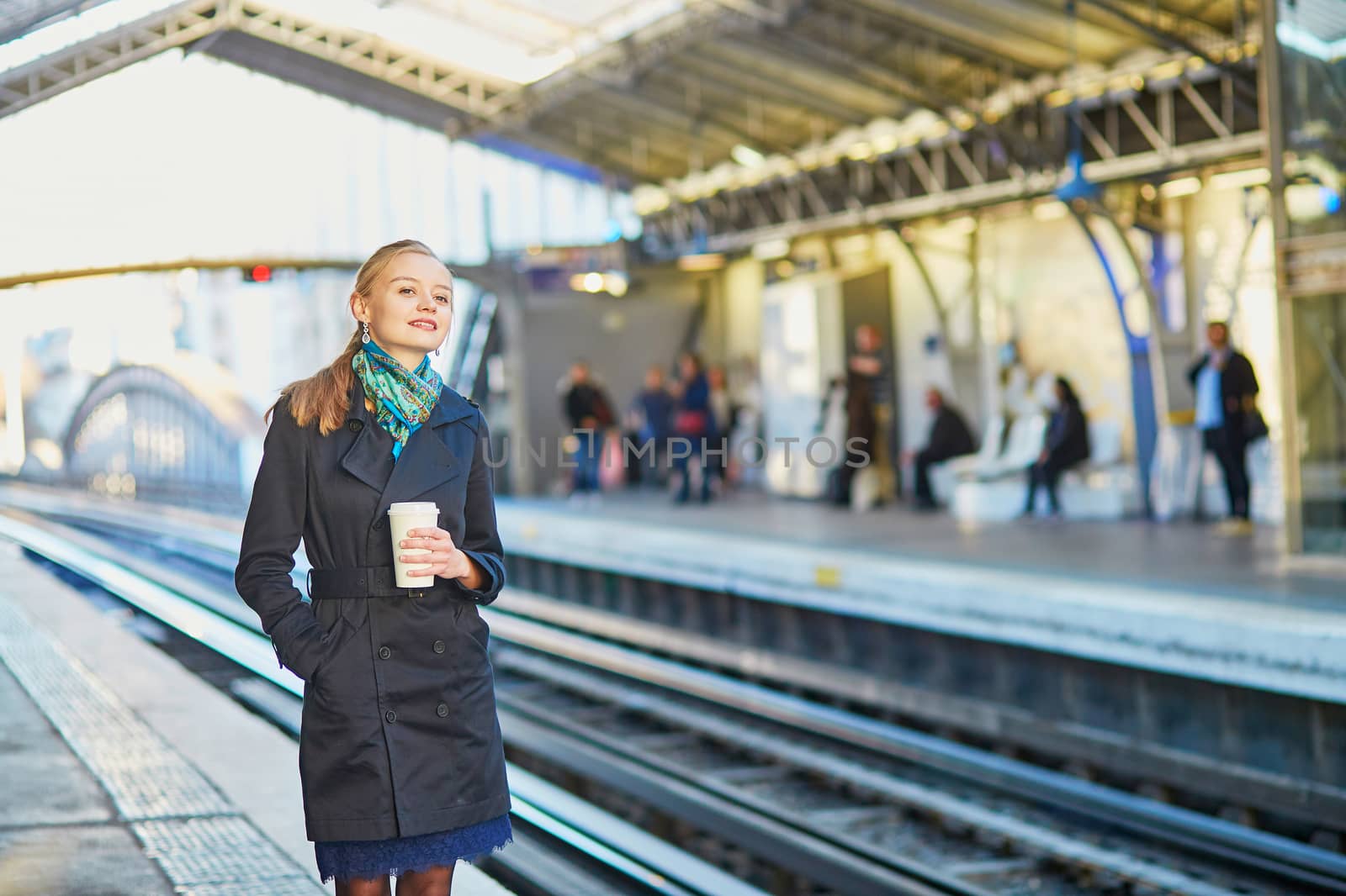 Beautiful young woman waiting for a train while drinking coffee on the platform of Parisian underground