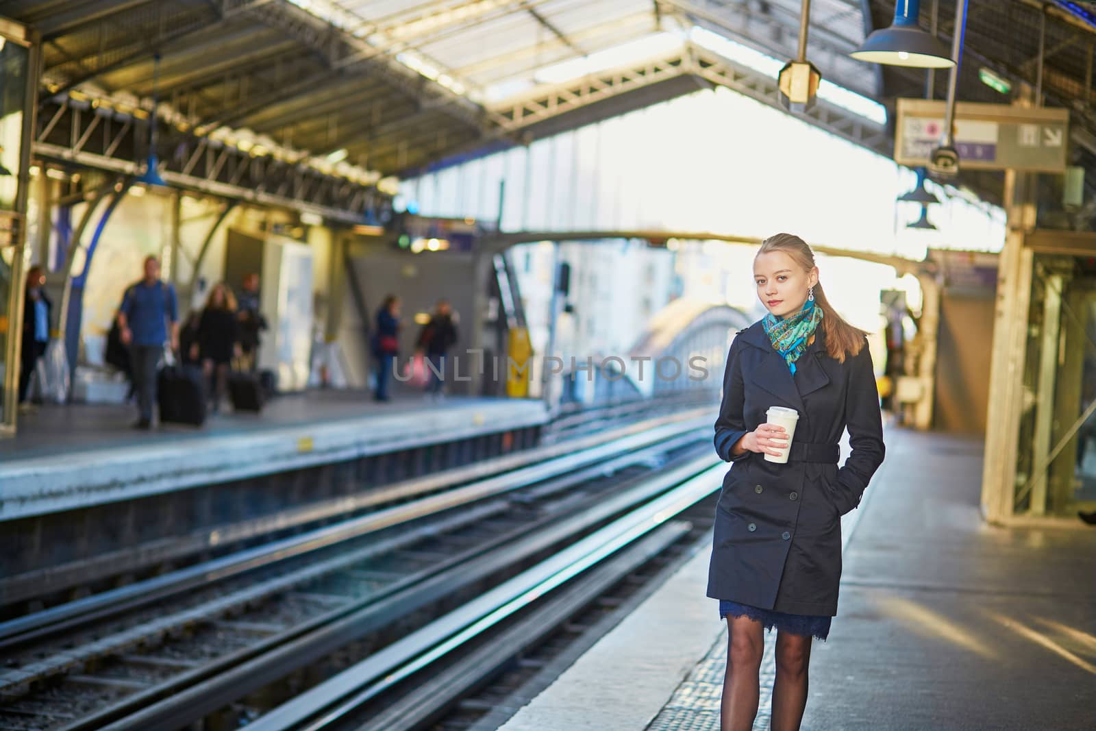 Beautiful young woman waiting for a train while drinking coffee on the platform of Parisian underground