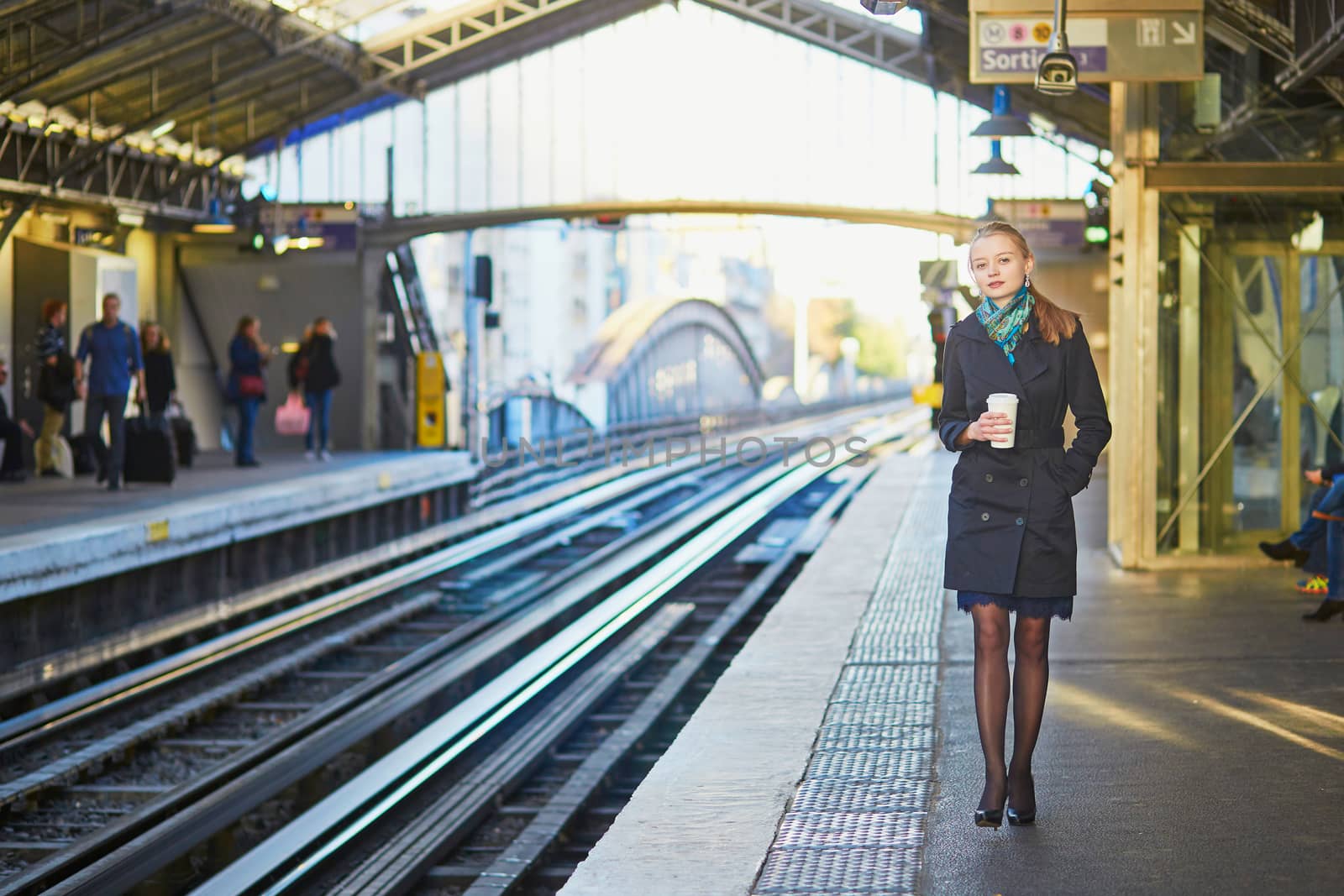 Beautiful young woman waiting for a train while drinking coffee on the platform of Parisian underground