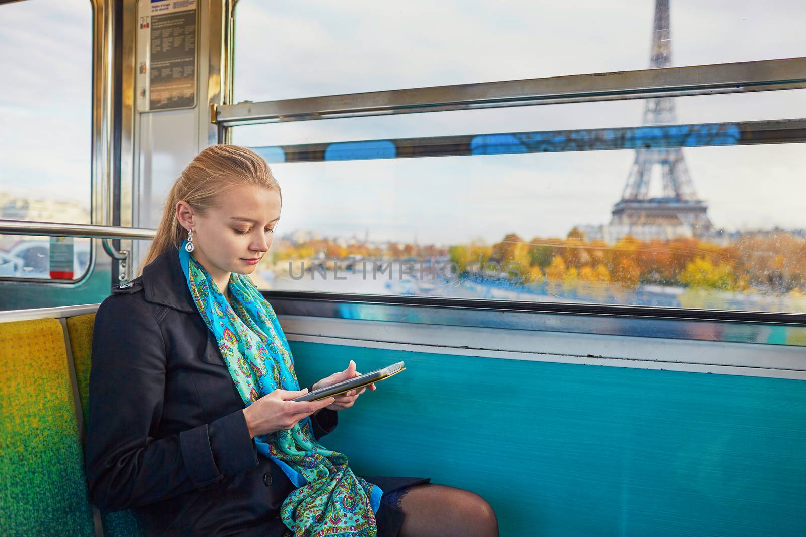 Beautiful young woman travelling in a train of Parisian underground and reading a book. Eiffel tower is behind the window
