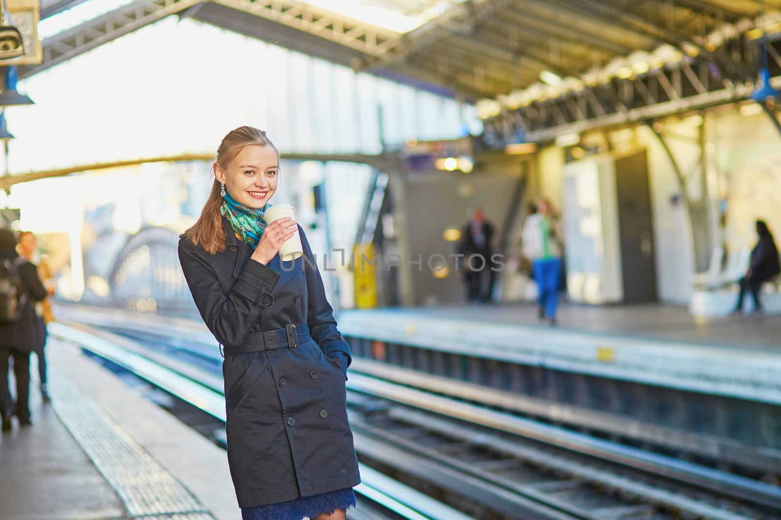 Beautiful young woman waiting for a train while drinking coffee on the platform of Parisian underground