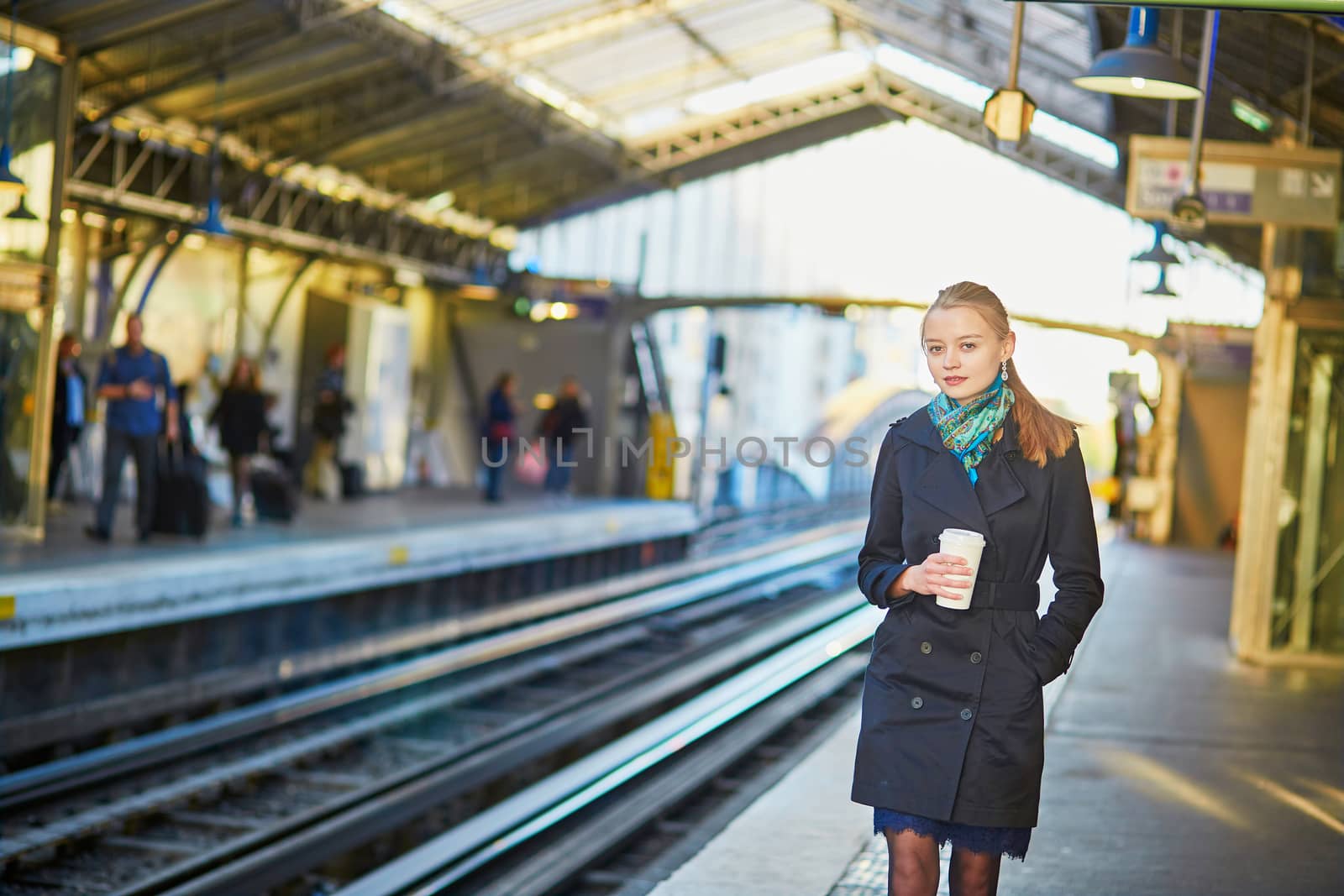Beautiful young woman waiting for a train while drinking coffee on the platform of Parisian underground