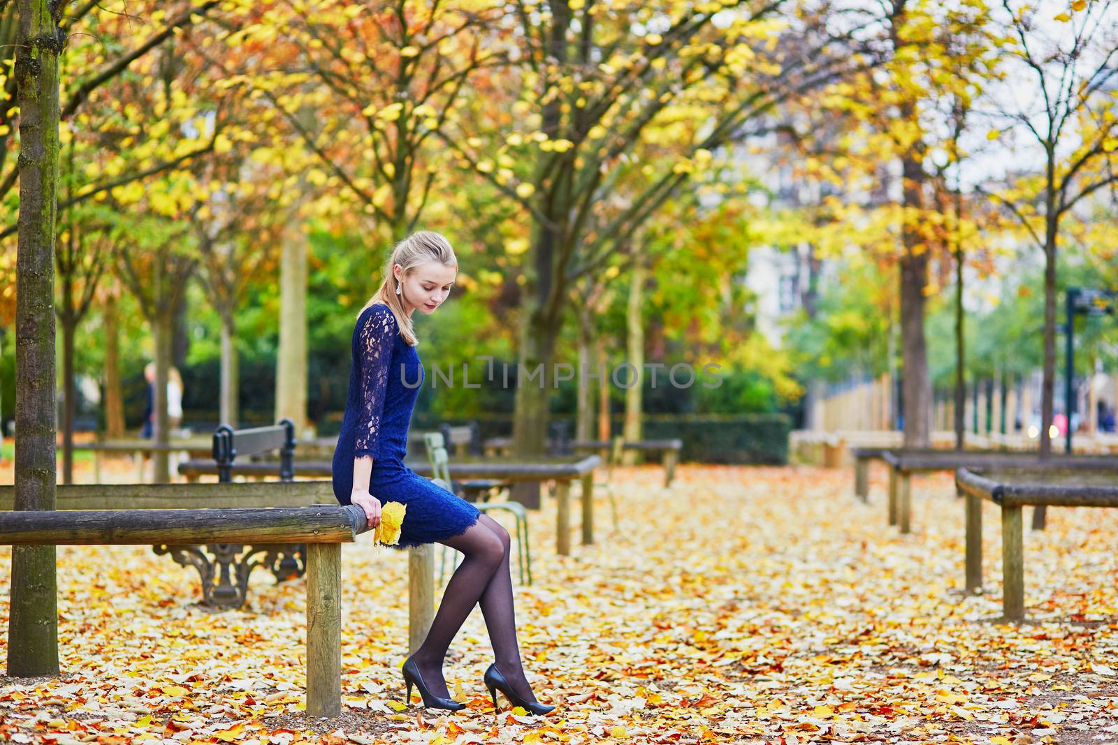 Beautiful young woman in blue dress in the Luxembourg garden of Paris on a fall day