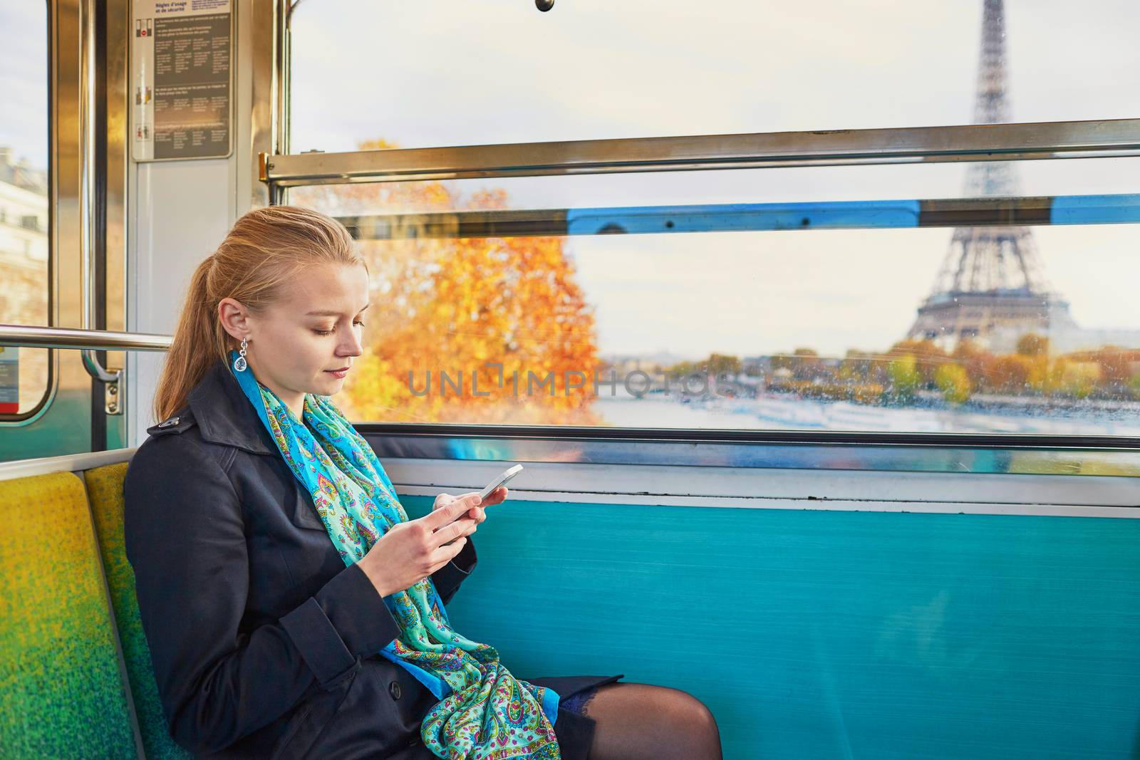 Beautiful young woman travelling in a train of Parisian underground and using her mobile phone. Eiffel tower is behind the window