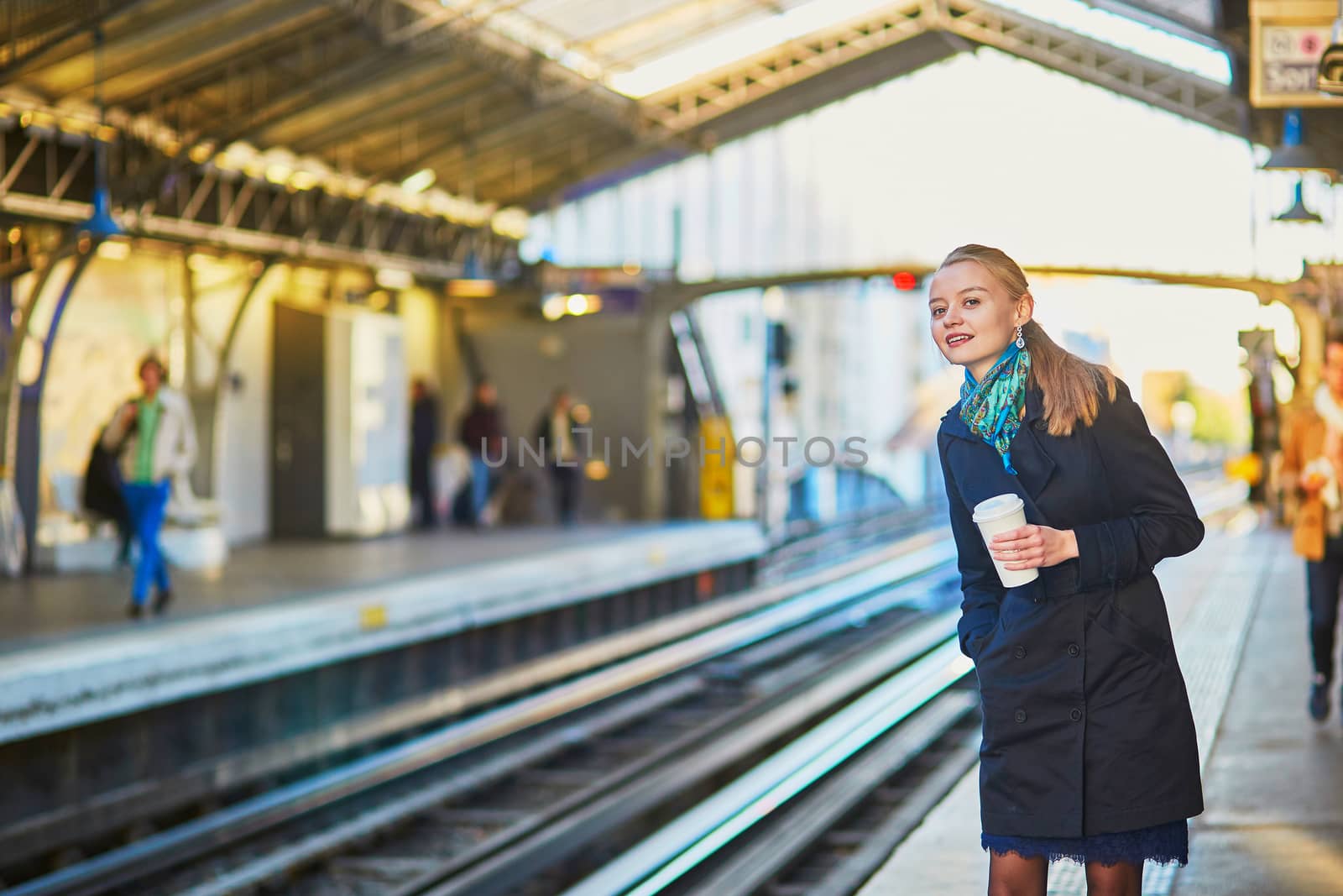 Beautiful young woman waiting for a train while drinking coffee on the platform of Parisian underground