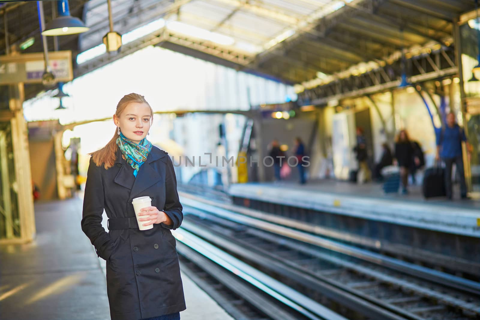 Beautiful young woman waiting for a train while drinking coffee on the platform of Parisian underground
