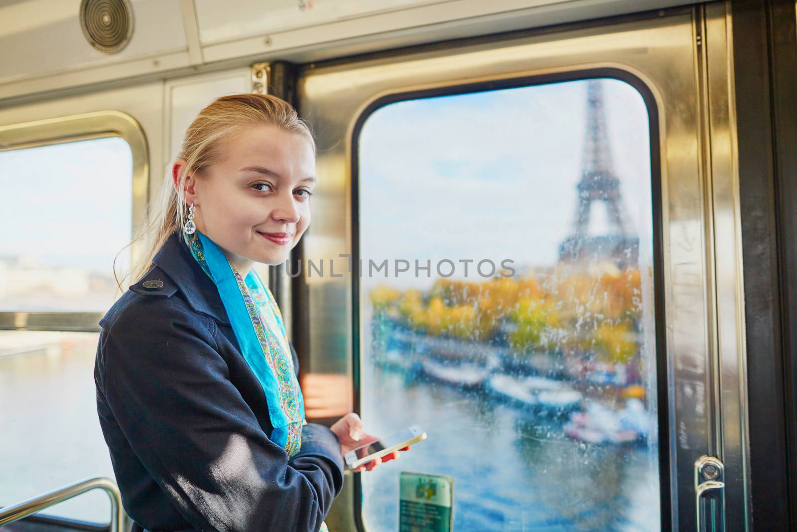 Beautiful young woman travelling in a train of Parisian underground and using her mobile phone. Eiffel tower is behind the window