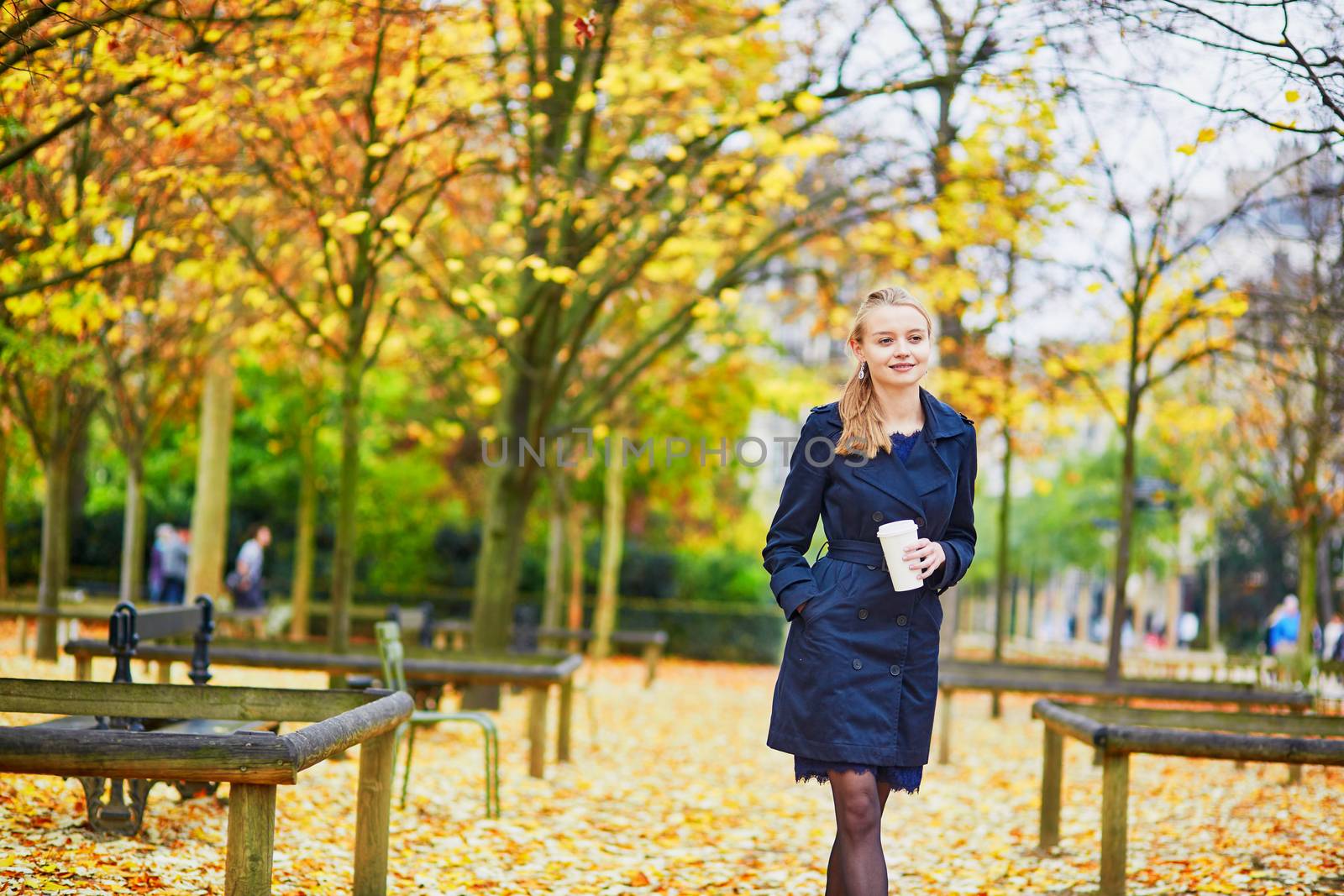 Beautiful young woman in the Luxembourg garden of Paris on a fall day, drinking coffee to go