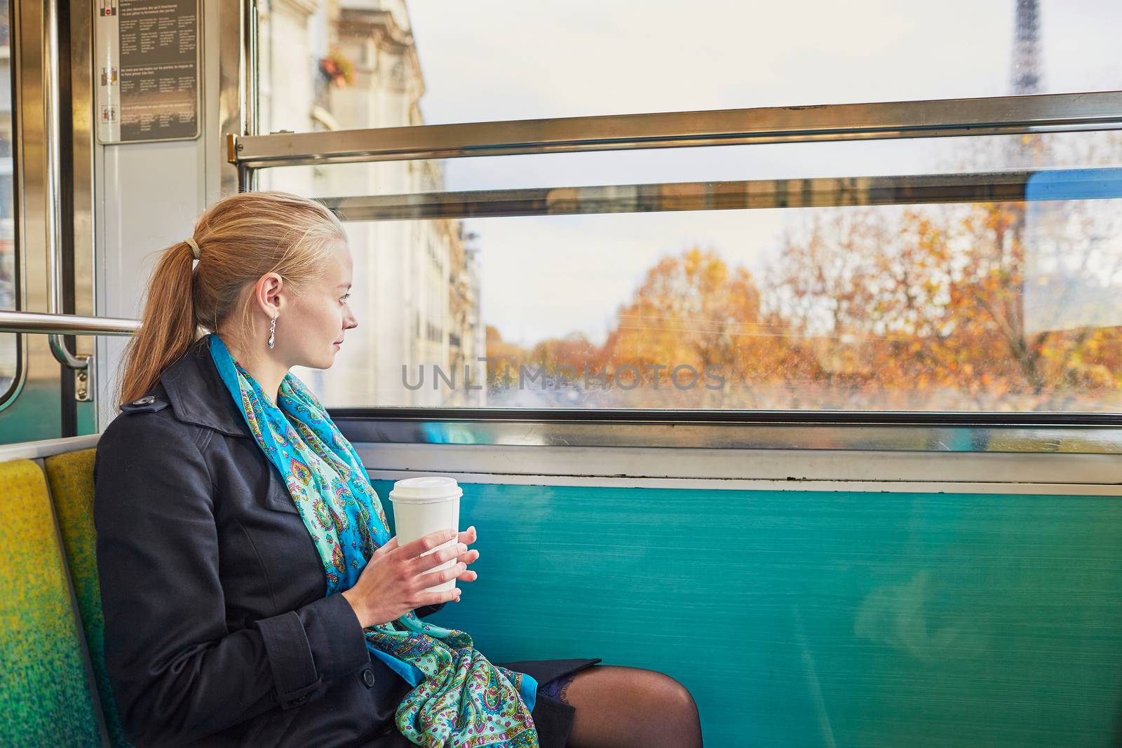 Beautiful young woman travelling in a train of Parisian underground and drinking coffee. Eiffel tower is behind the window