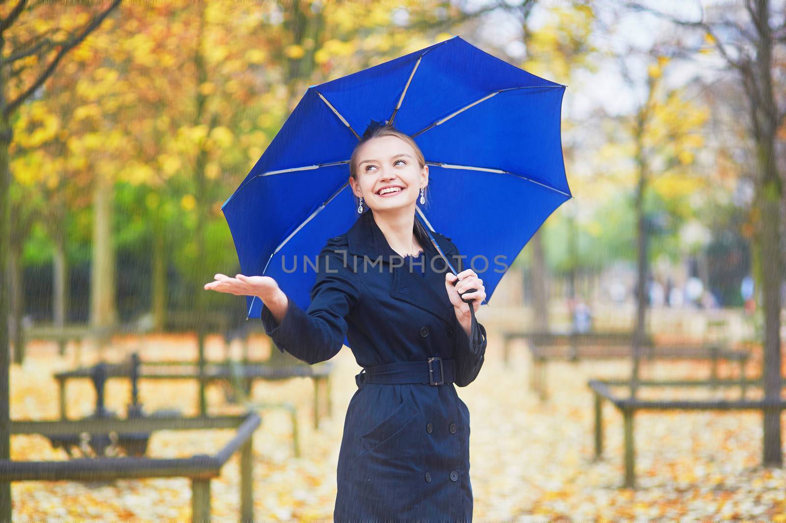 Beautiful young woman with blue umbrella in the Luxembourg garden of Paris on a fall or spring rainy day
