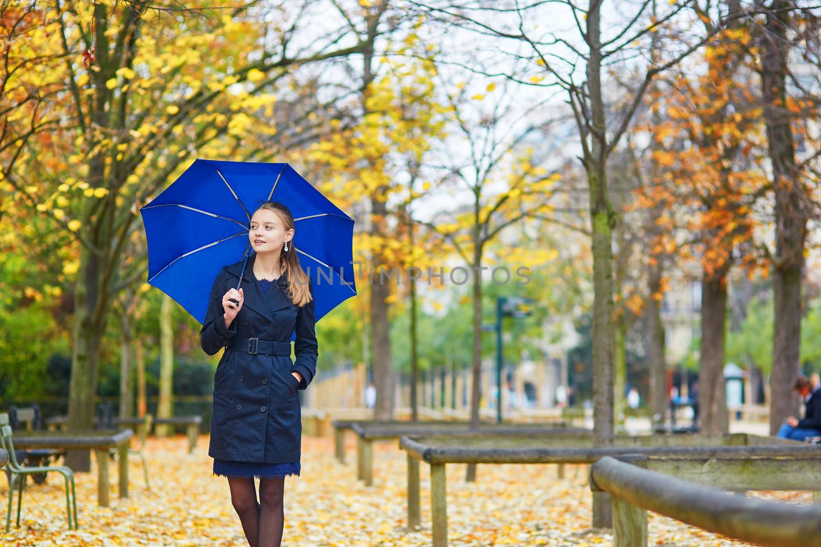 Beautiful young woman with blue umbrella in the Luxembourg garden of Paris on a fall or spring rainy day
