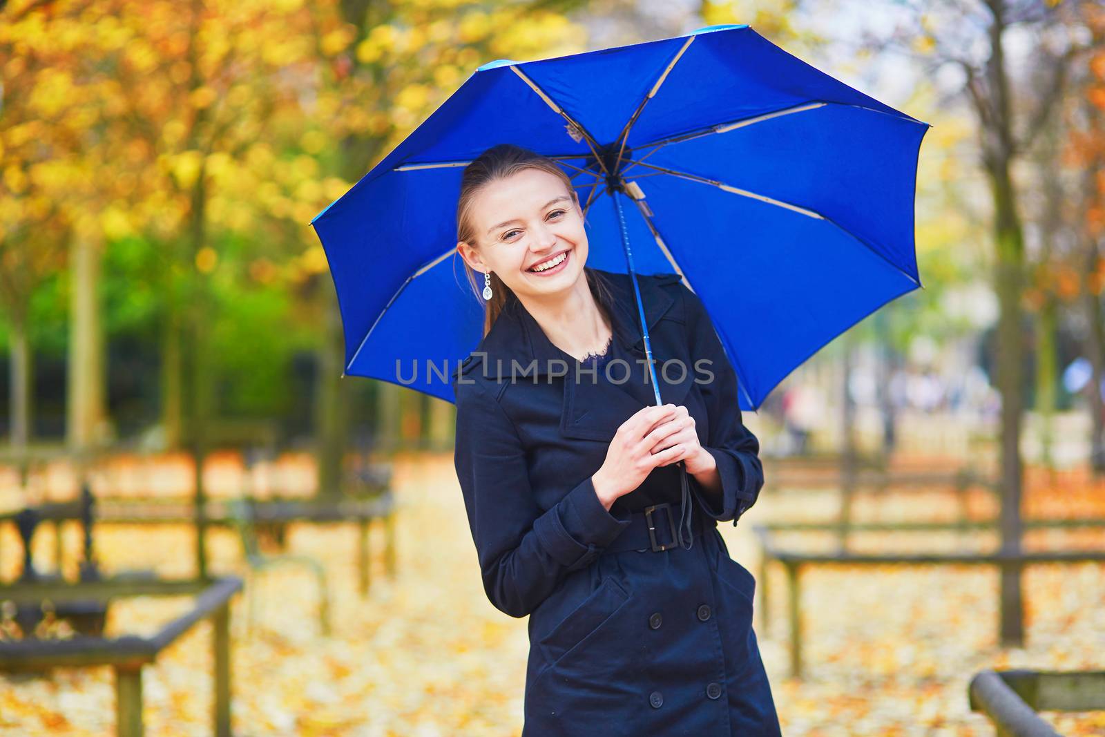 Beautiful young woman with blue umbrella in the Luxembourg garden of Paris on a fall day