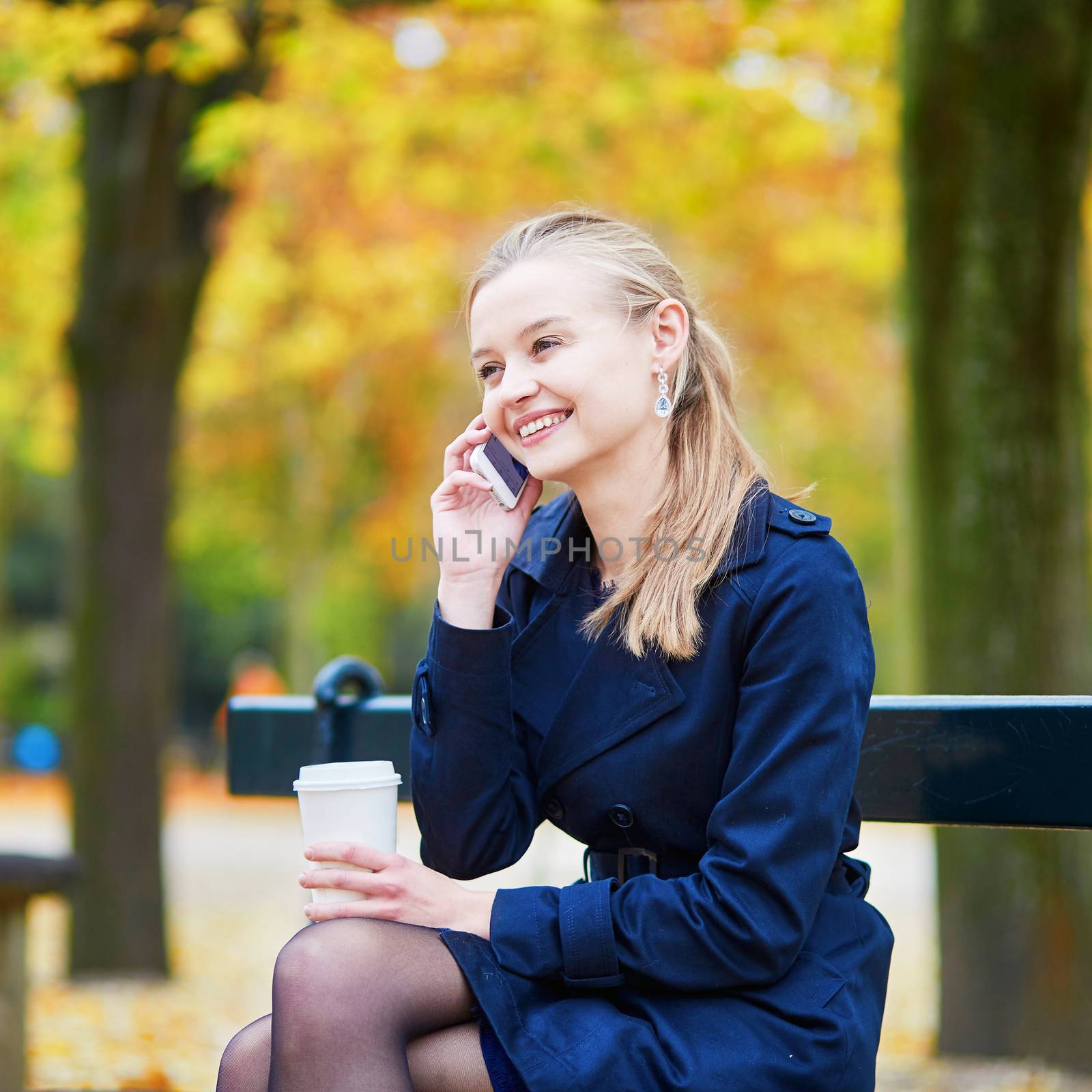 Beautiful young woman drinking coffee and speaking on the phone in the Luxembourg garden of Paris on a fall day