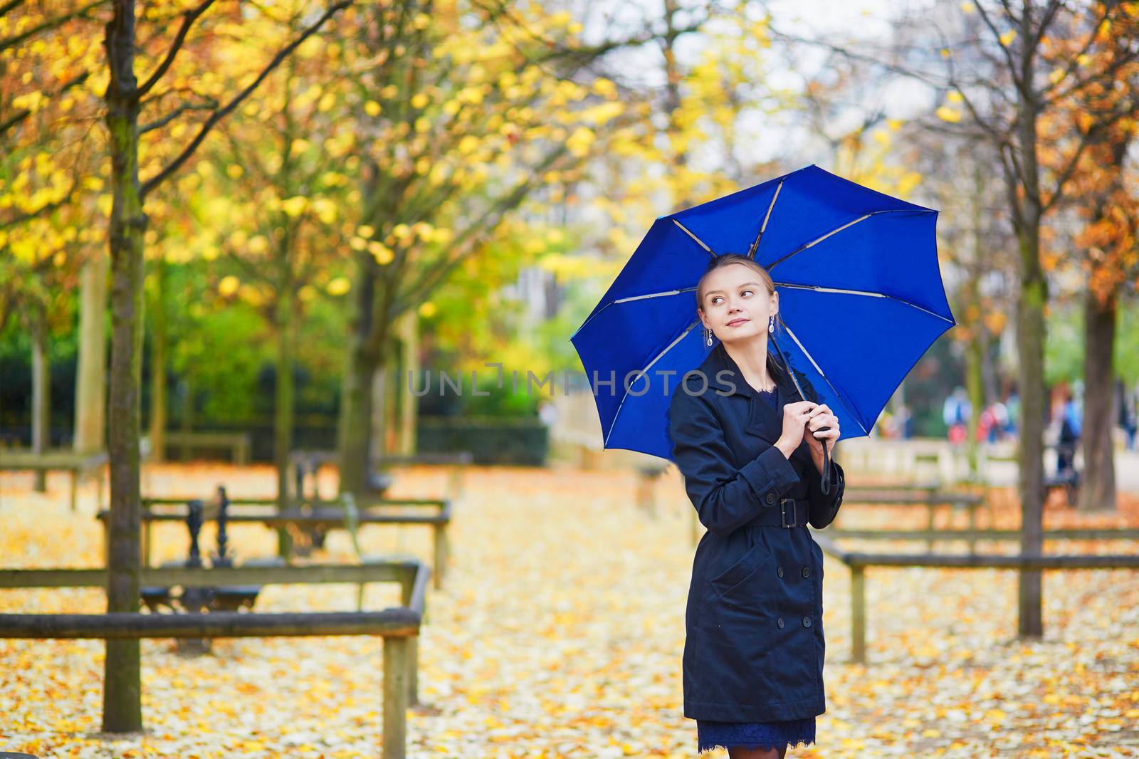 Beautiful young woman with blue umbrella in the Luxembourg garden of Paris on a fall or spring rainy day