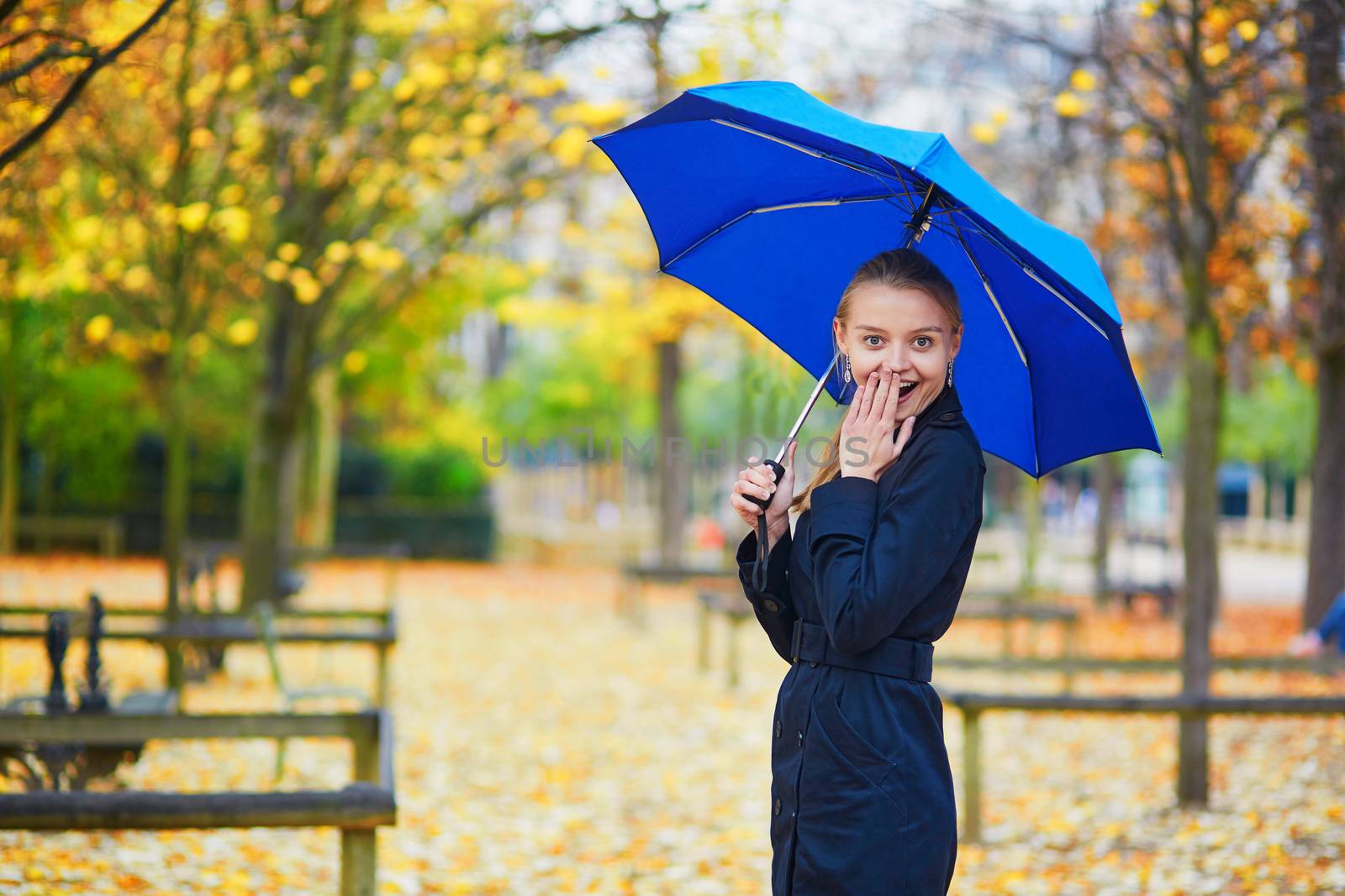 Beautiful young woman with blue umbrella in the Luxembourg garden of Paris on a fall or spring rainy day