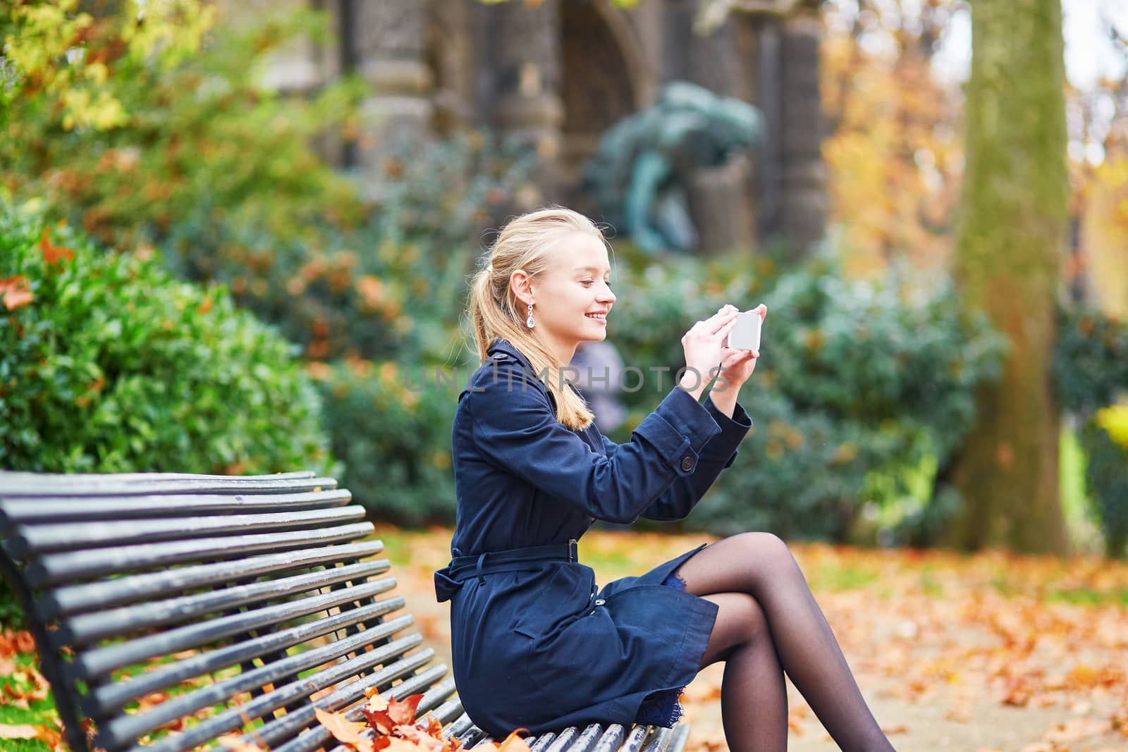 Beautiful young woman on a street of Paris on a sunny fall or spring day taking selfie with her mobile phone