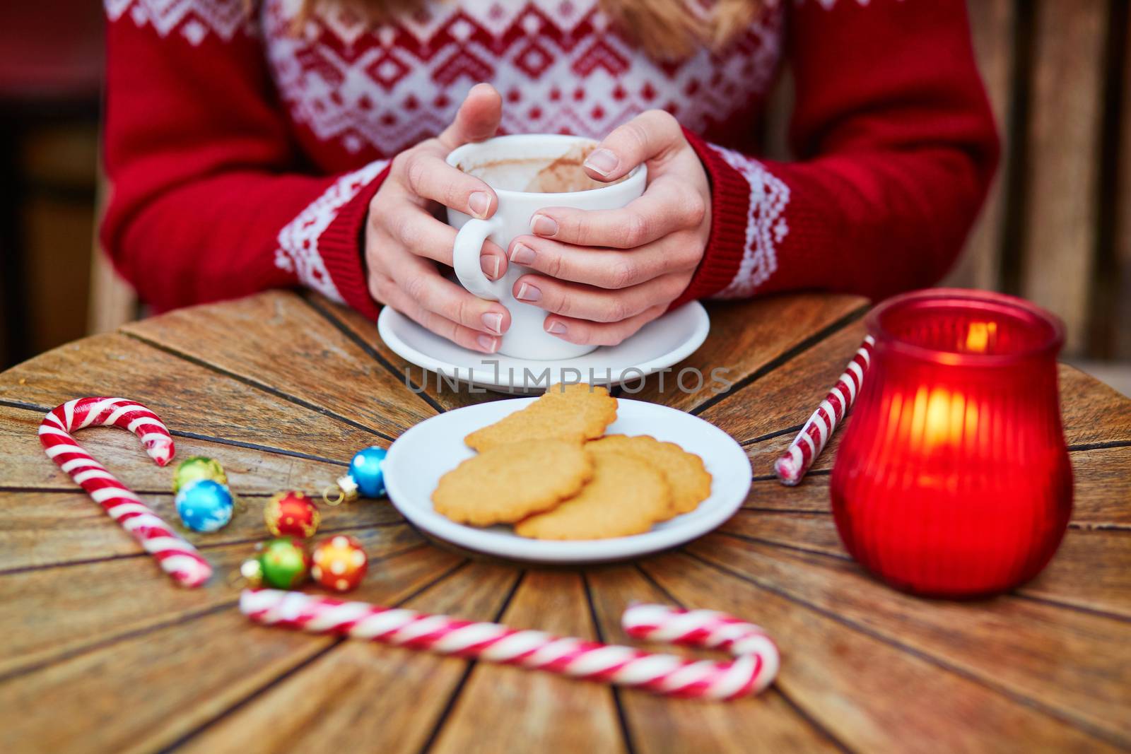 Cheerful young woman drinking hot chocolate in a cozy outdoor Parisian cafe decorated for Christmas