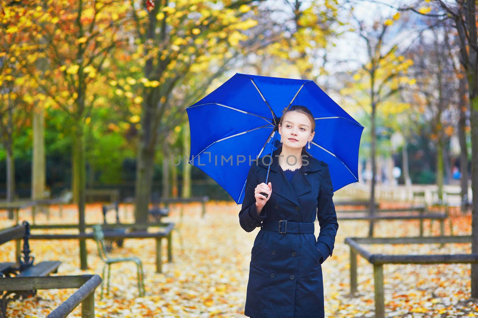 Beautiful young woman with blue umbrella in the Luxembourg garden of Paris on a fall or spring rainy day