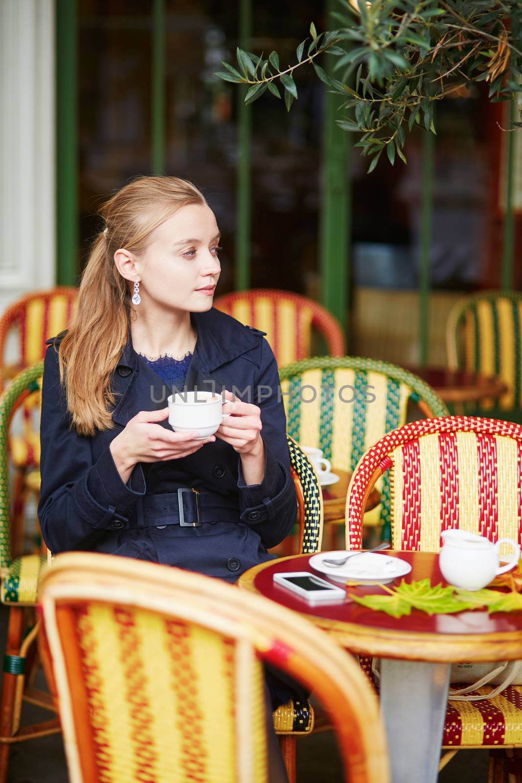 Beautiful young woman drinking hot chocolate in Parisian outdoor cafe on a nice fall day