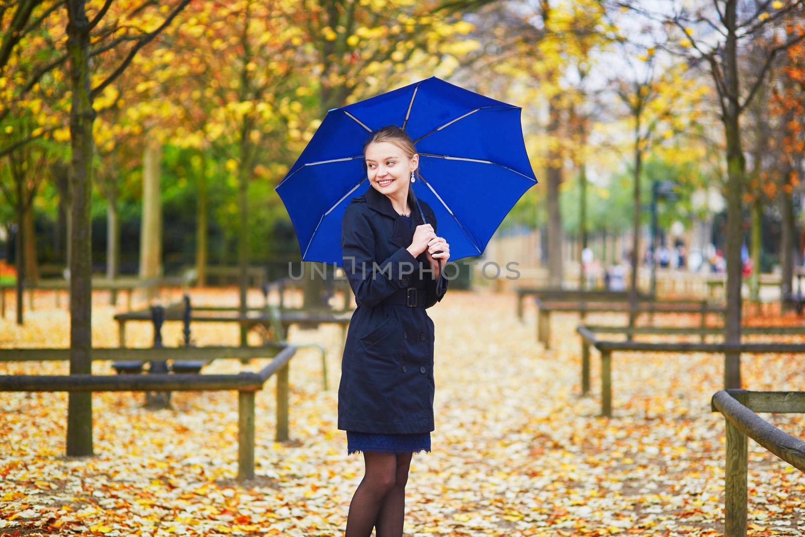Beautiful young woman with blue umbrella in the Luxembourg garden of Paris on a fall or spring rainy day