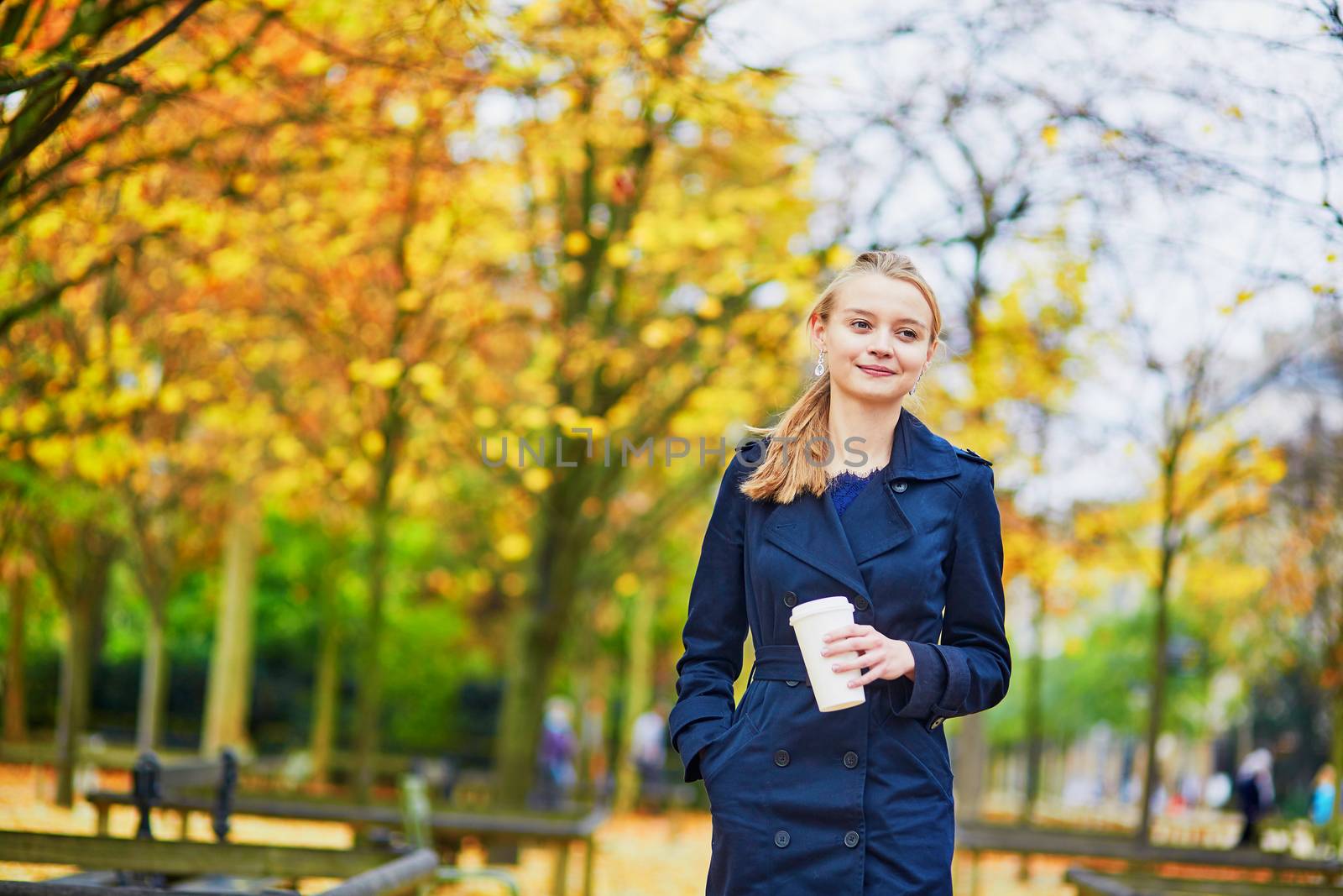 Beautiful young woman in the Luxembourg garden of Paris on a fall day, drinking coffee to go