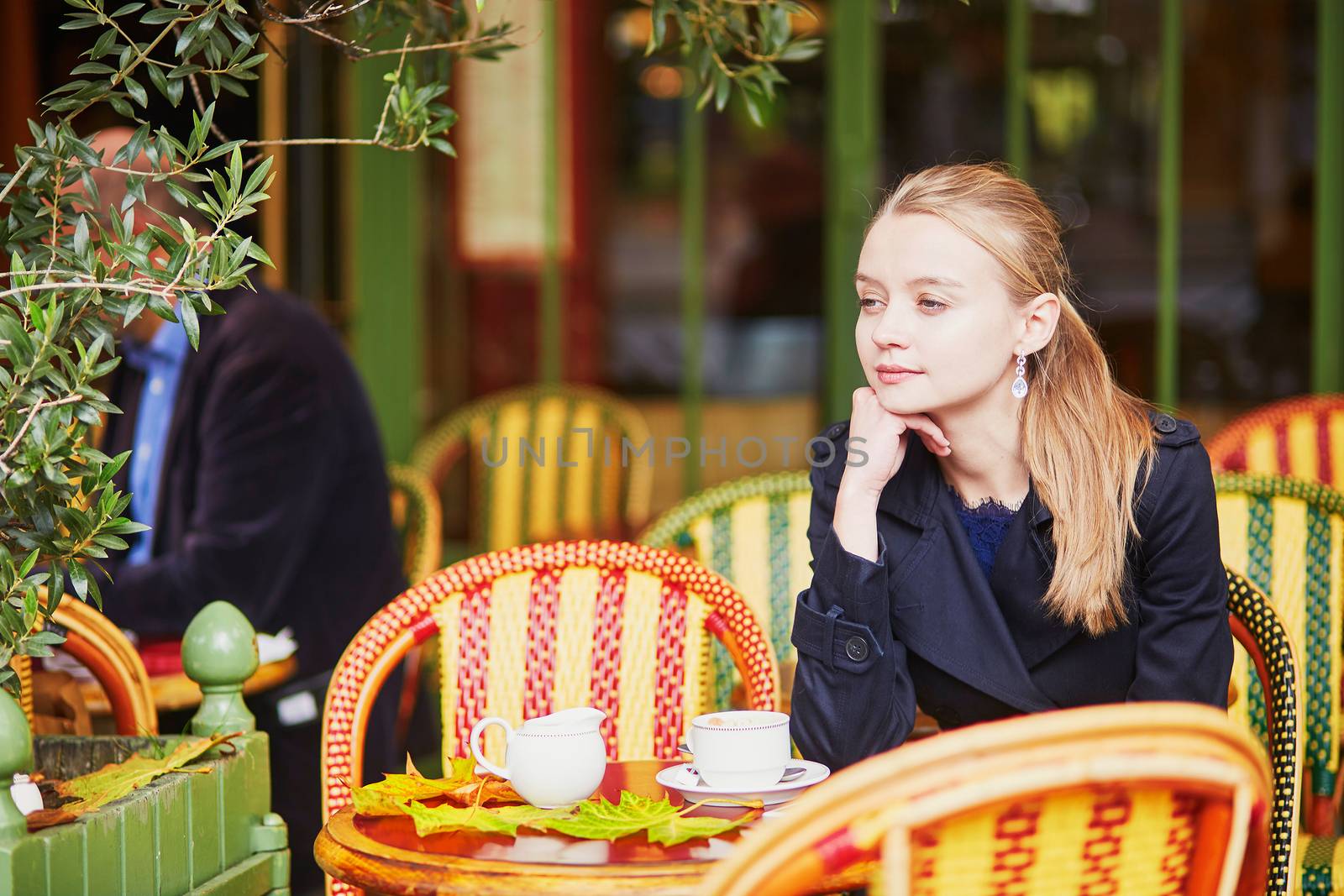 Beautiful young woman drinking hot chocolate in Parisian outdoor cafe on a nice fall day