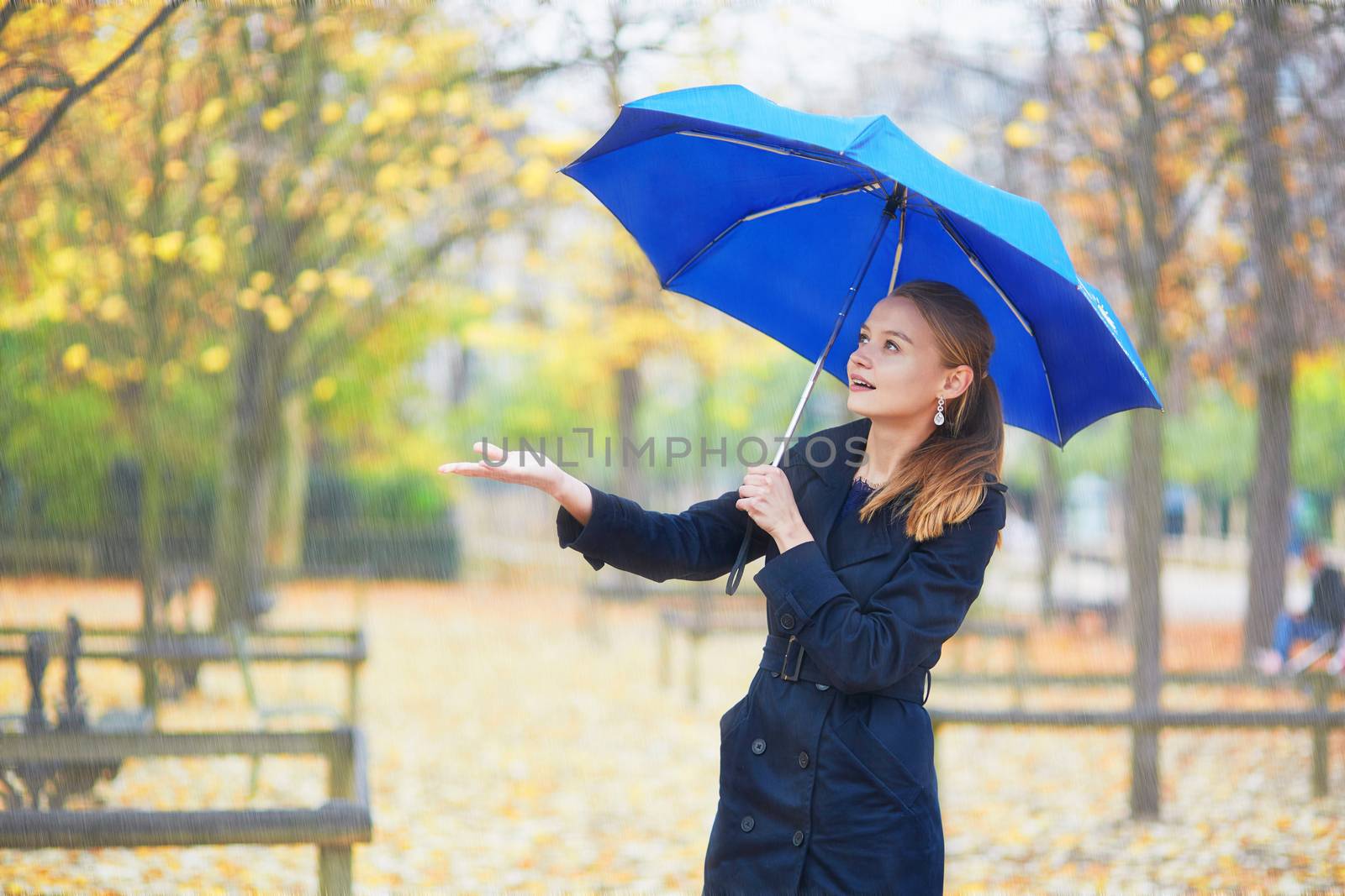 Beautiful young woman with blue umbrella in the Luxembourg garden of Paris on a fall or spring rainy day