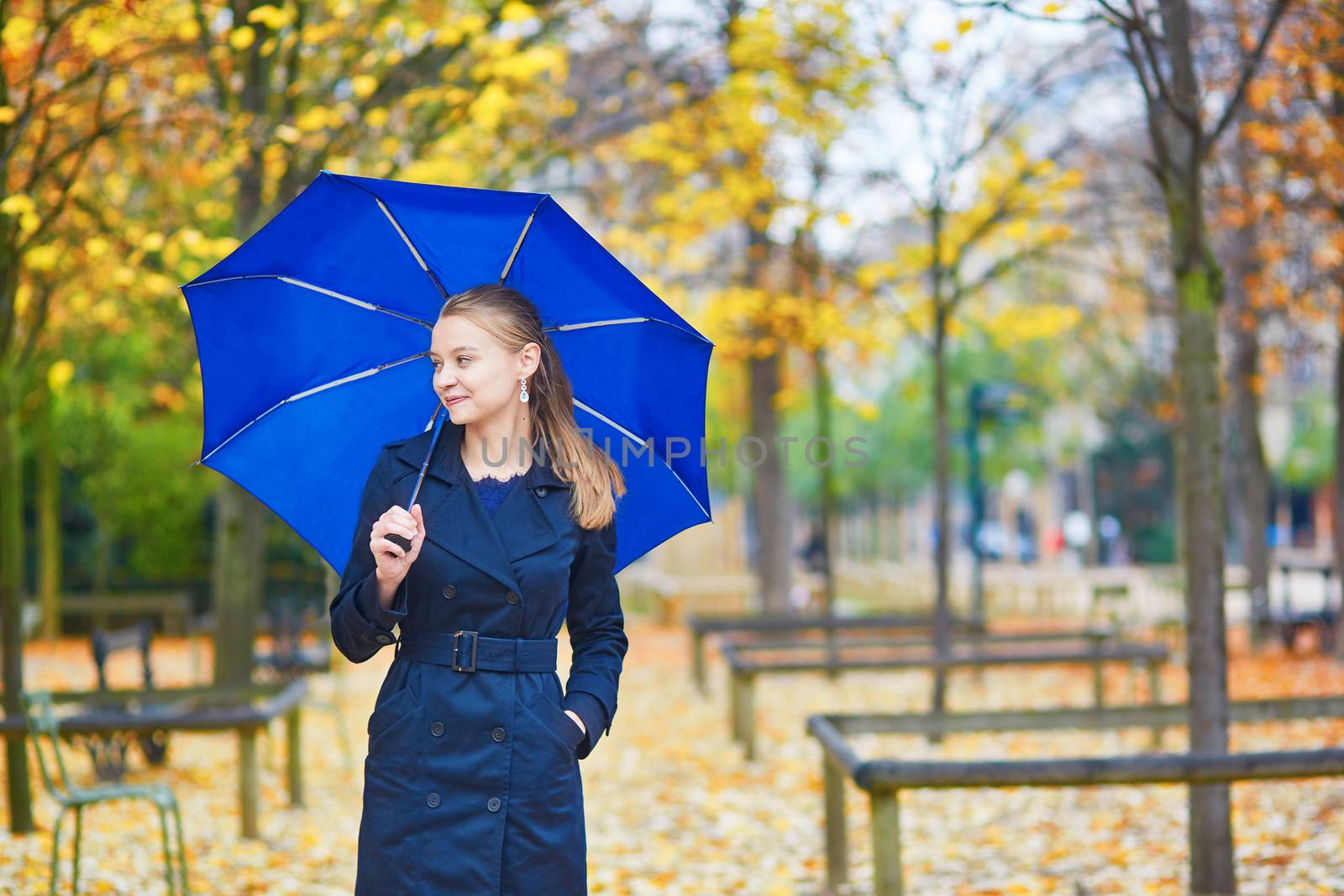Beautiful young woman with blue umbrella in the Luxembourg garden of Paris on a fall or spring rainy day
