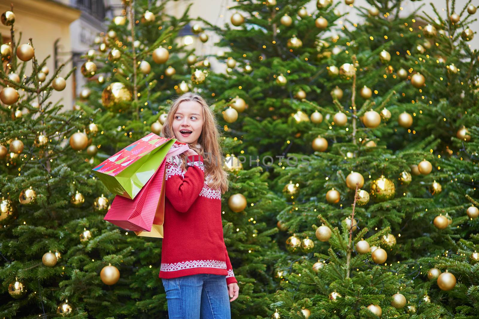 Cheerful young woman on a street of Paris decorated for Christmas with shopping bags