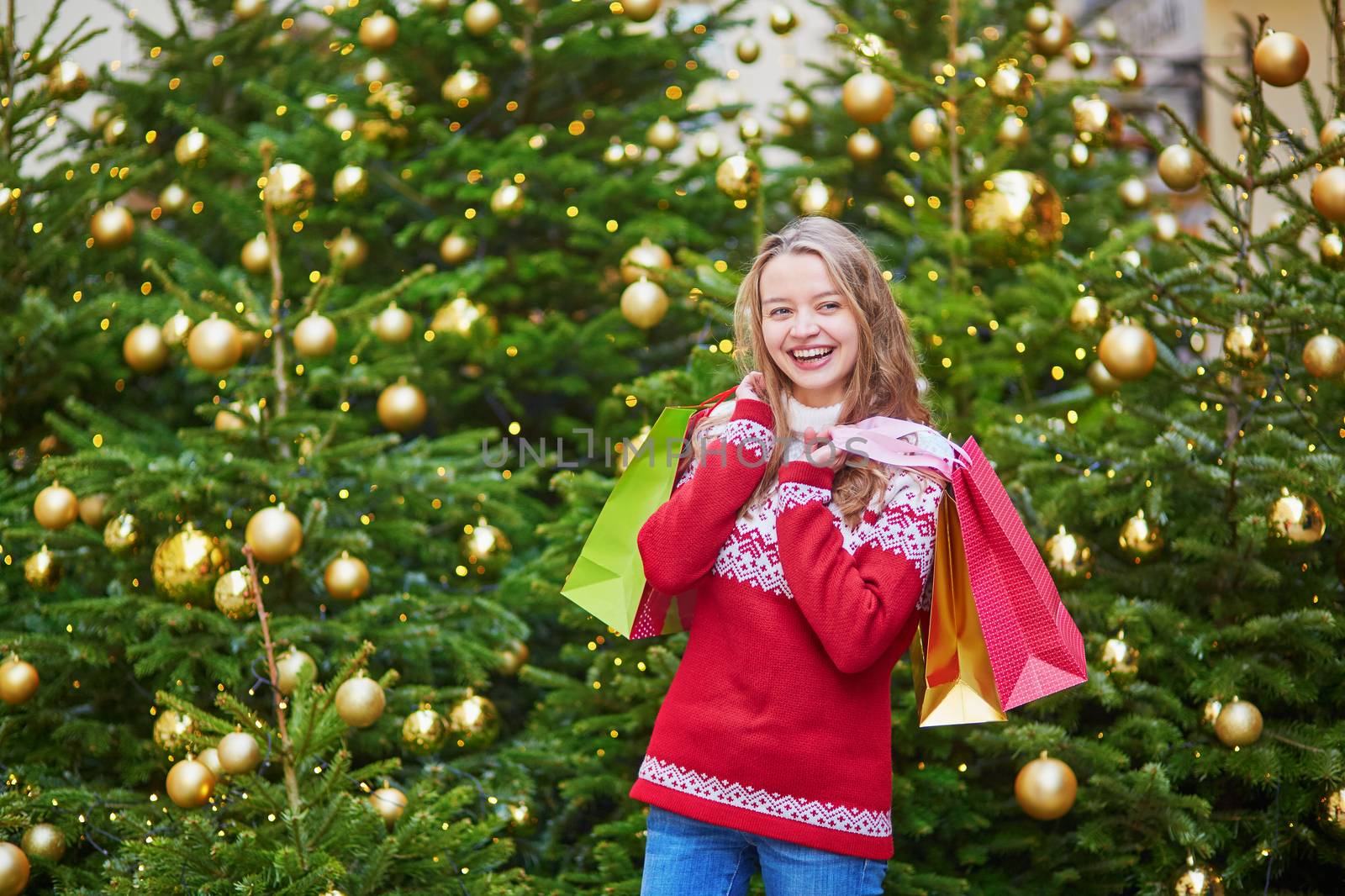 Cheerful young woman on a street of Paris decorated for Christmas with shopping bags