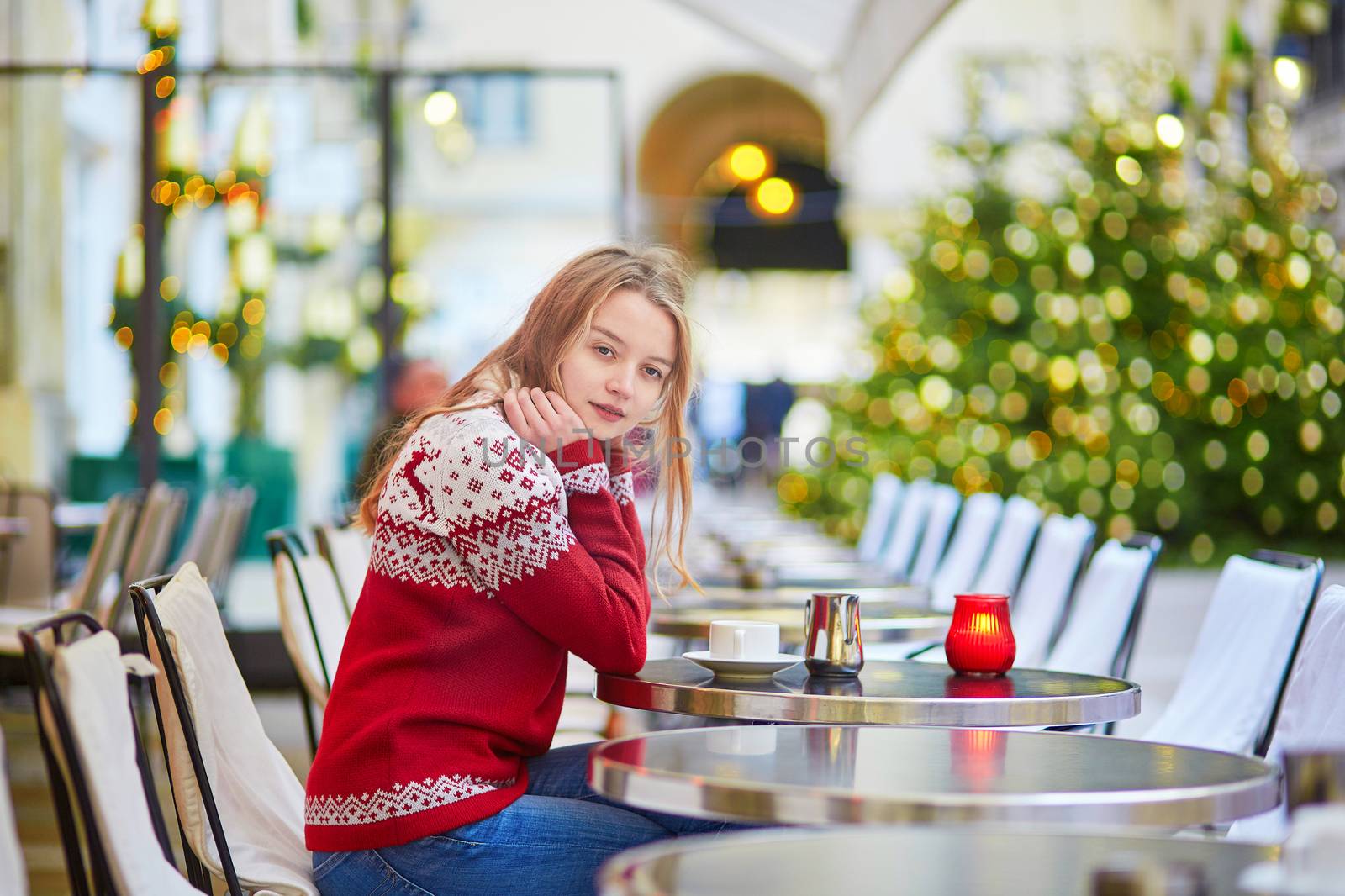 Cheerful young woman drinking hot chocolate in a cozy outdoor Parisian cafe decorated for Christmas