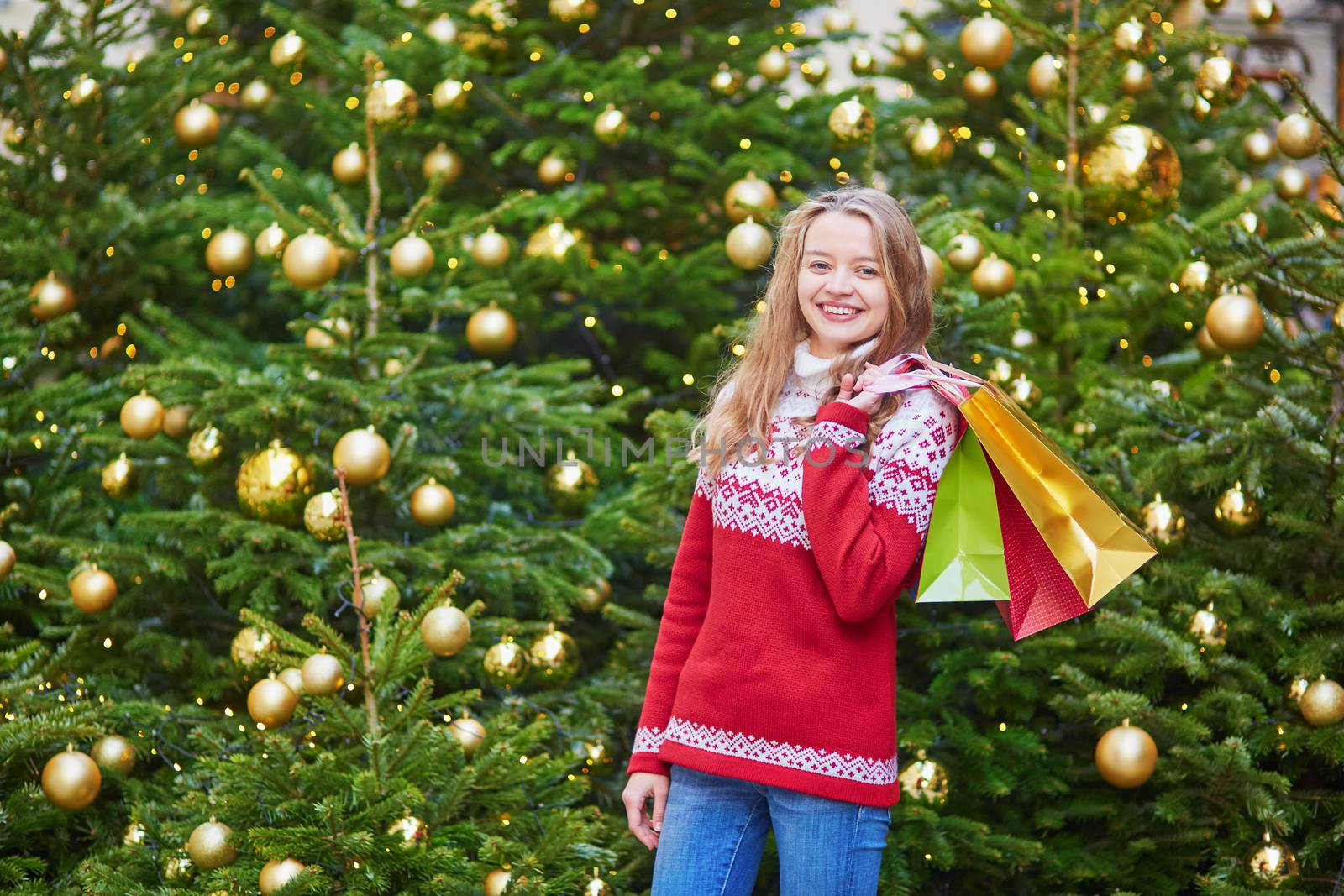Cheerful young woman on a street of Paris decorated for Christmas with shopping bags