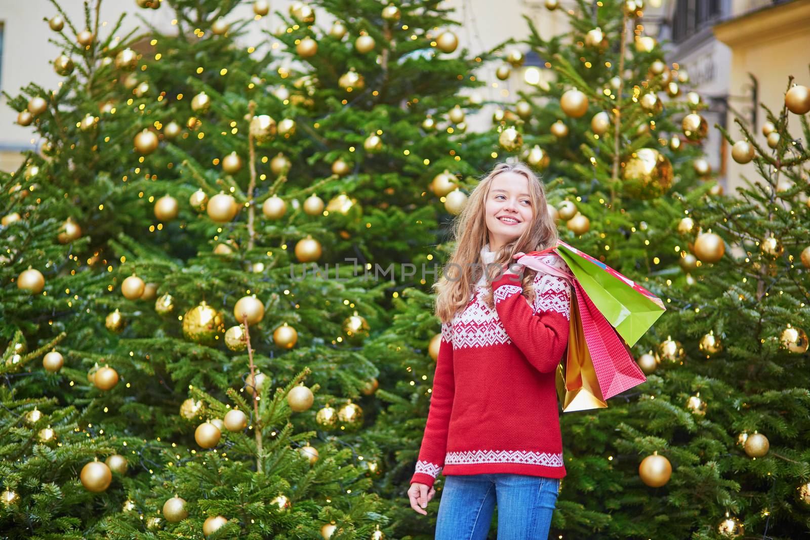 Cheerful young woman on a street of Paris decorated for Christmas with shopping bags