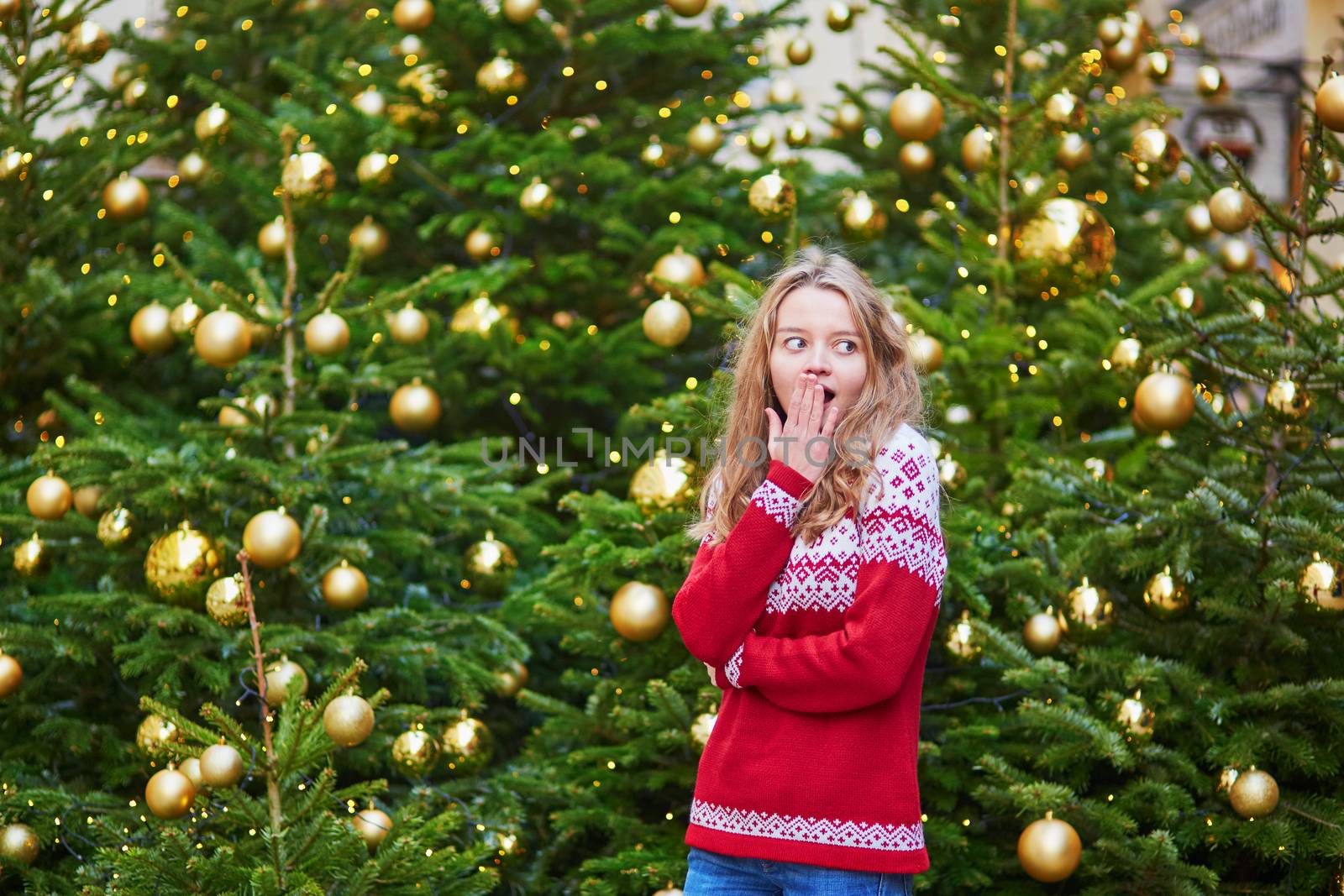 Cheerful young woman on a street of Paris decorated for Christmas with shopping bags