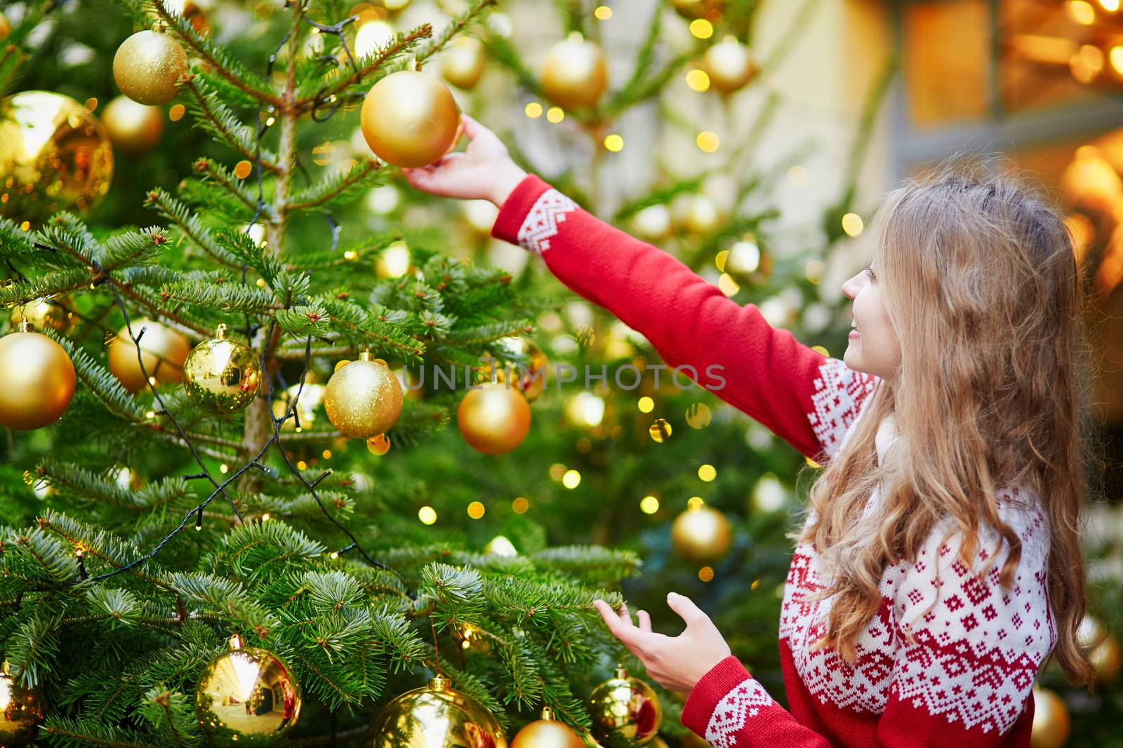 Cheerful young woman decorating Christmas tree with golden balls