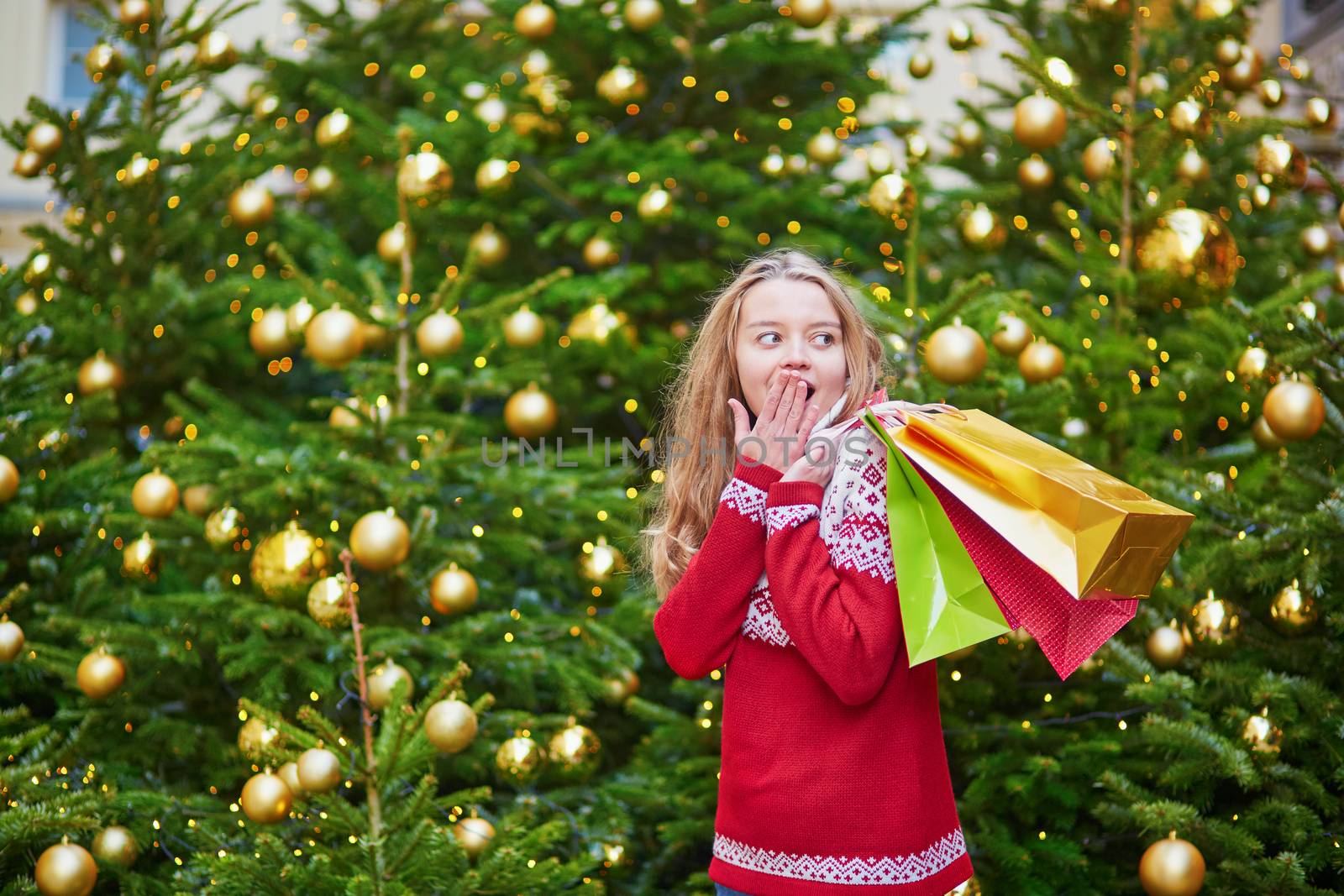 Cheerful young woman on a street of Paris decorated for Christmas with shopping bags