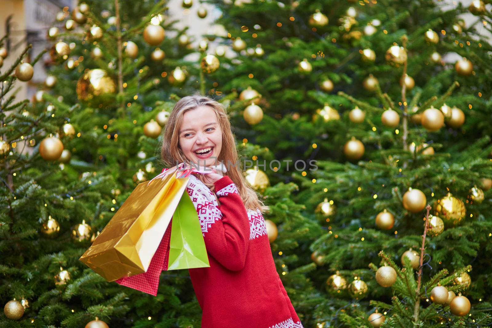 Cheerful young girl with colorful shopping bags near Christmas tree