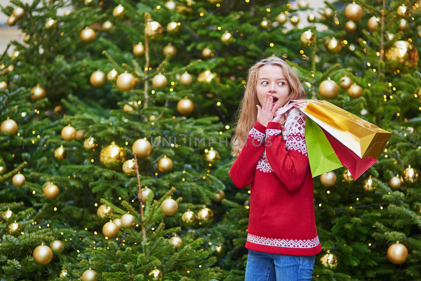 Cheerful young girl with colorful shopping bags near Christmas tree