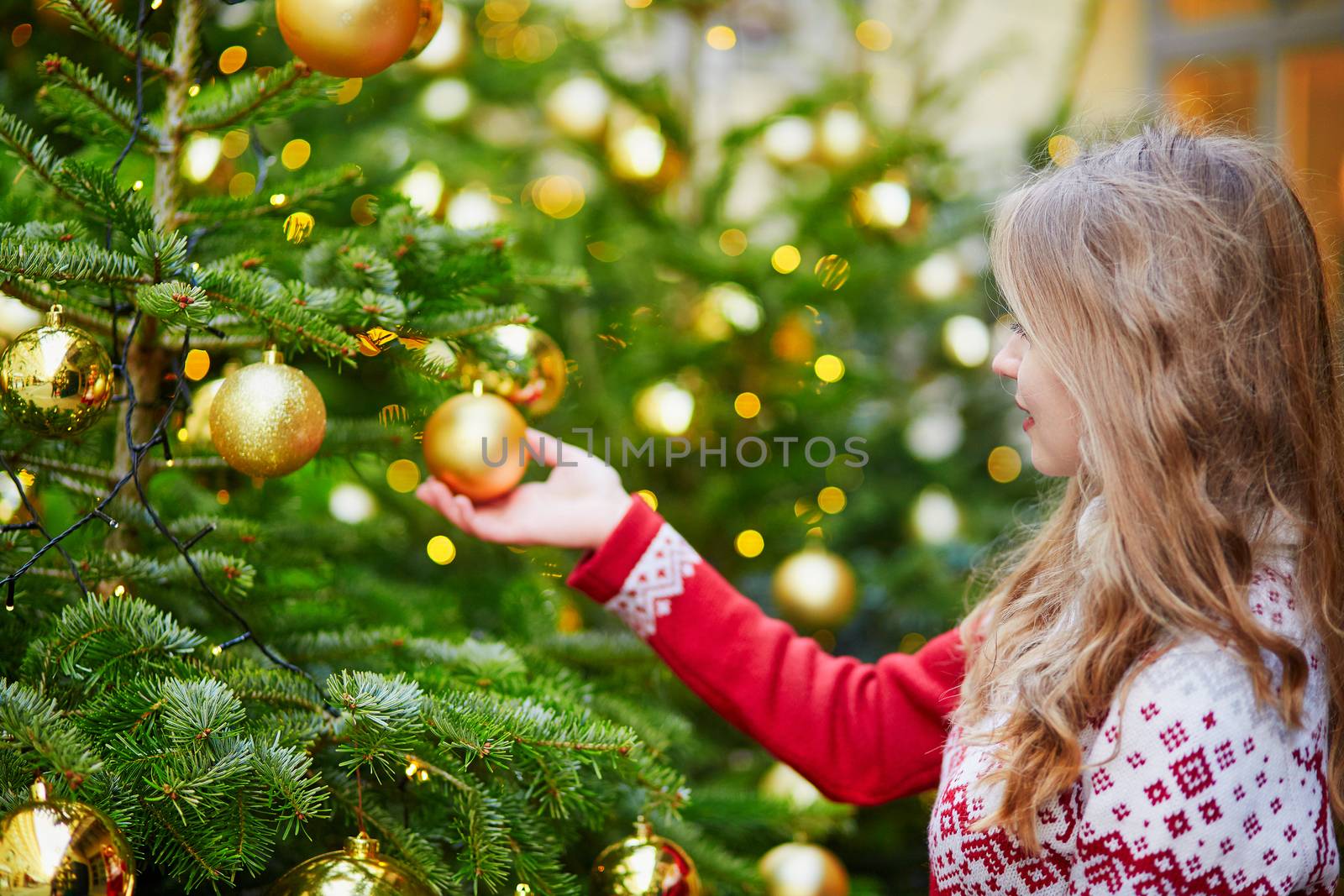 Cheerful young woman decorating Christmas tree with golden balls
