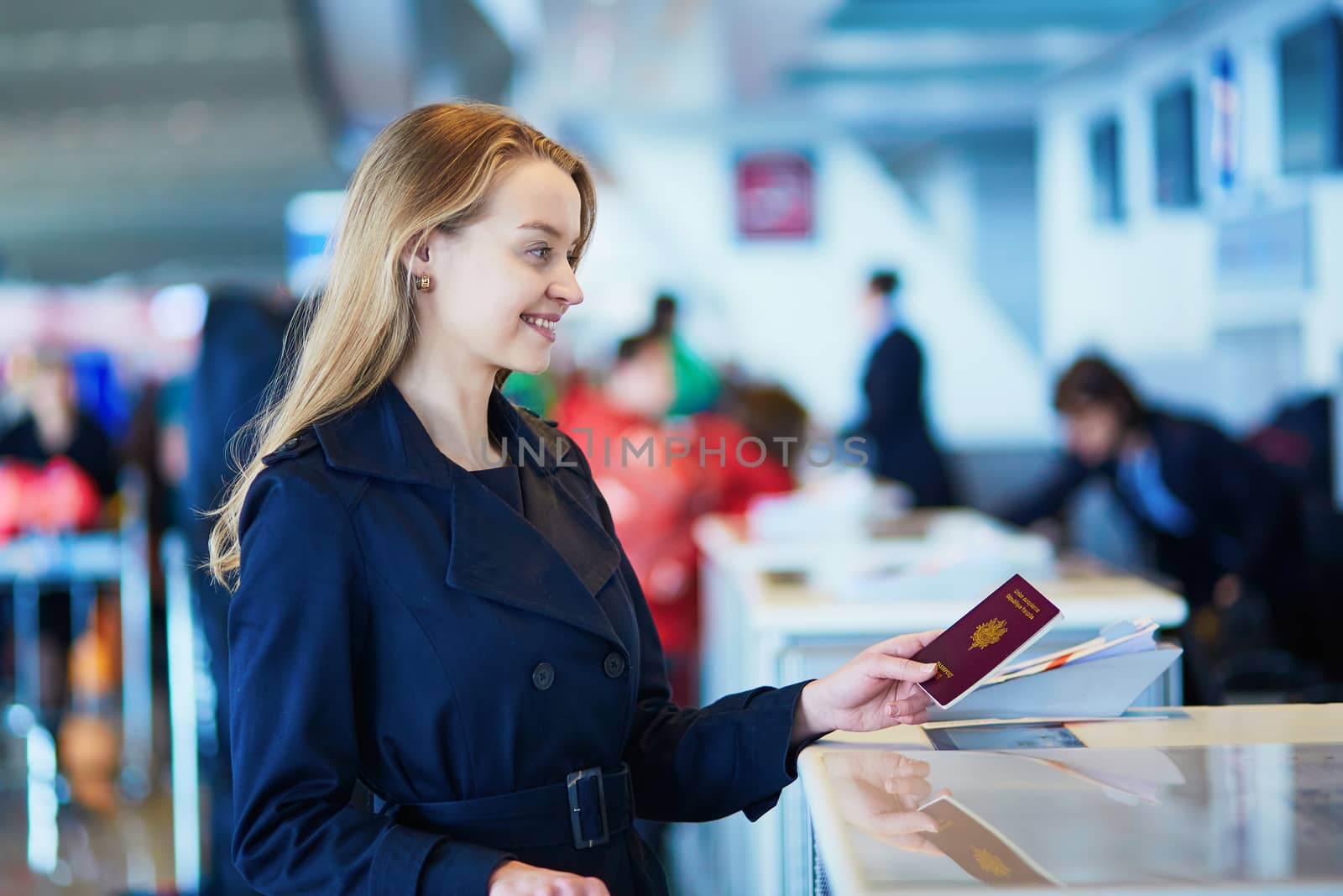 Young woman in international airport at check-in counter, giving her passport to an officer and waiting for her boarding pass