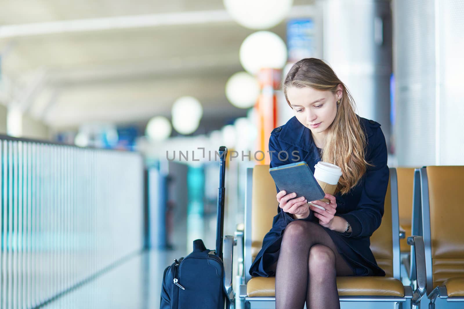 Young woman in international airport, reading and drinking coffee while waiting for her flight