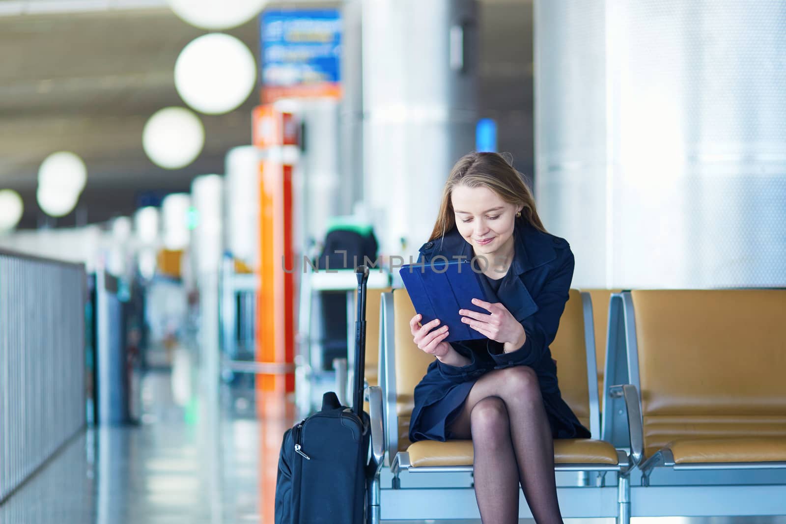 Young woman in international airport, waiting for her flight, using her tablet