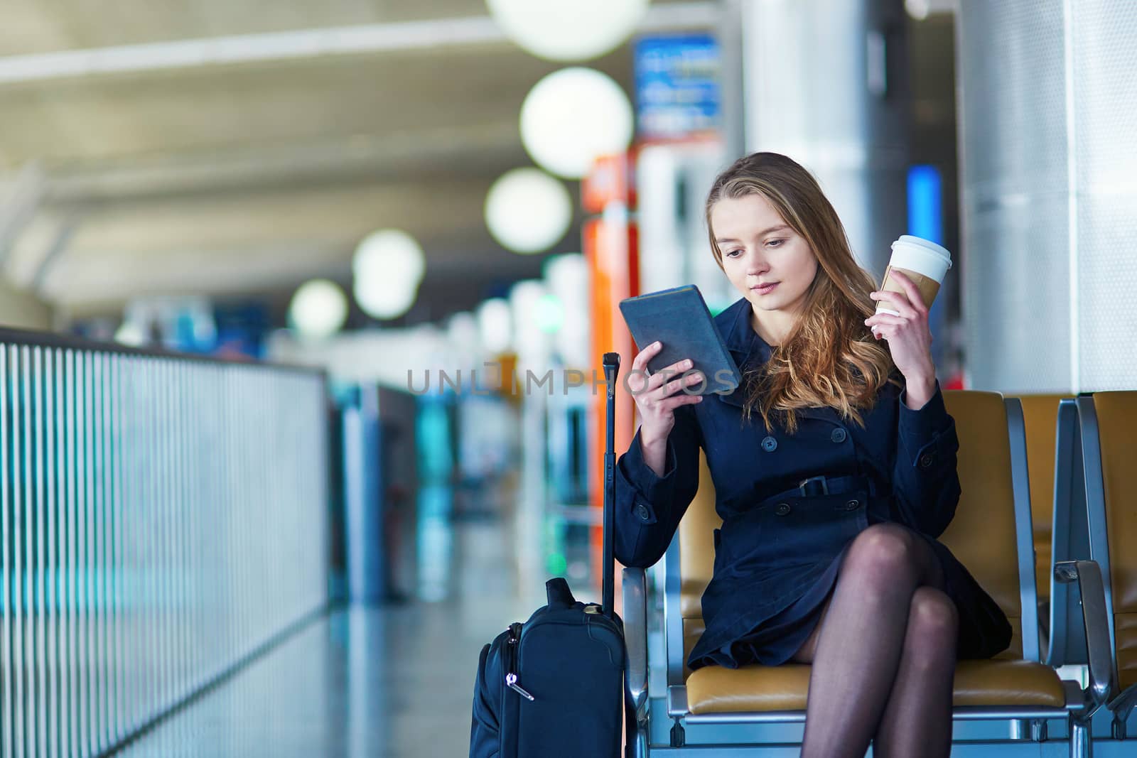 Young woman in international airport, reading and drinking coffee while waiting for her flight