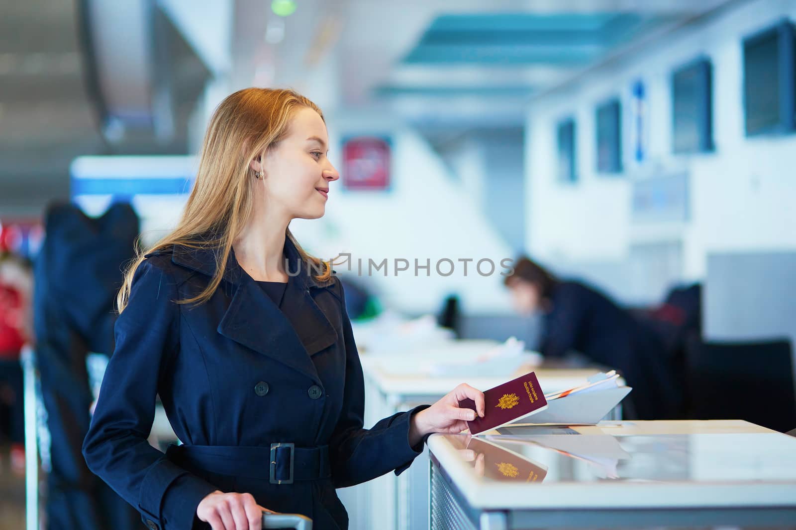 Young woman in international airport at check-in counter, giving her passport to an officer and waiting for her boarding pass